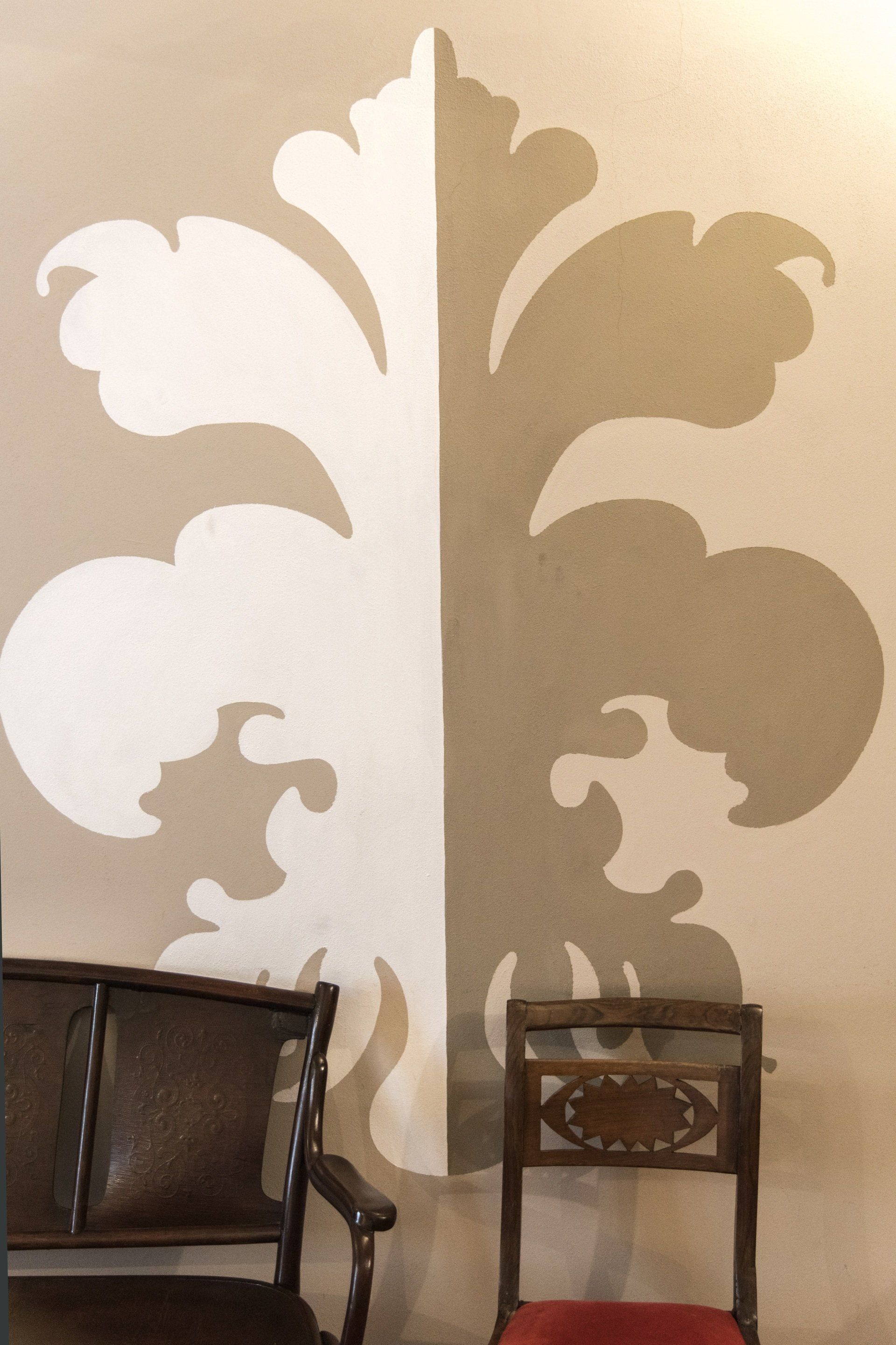 Decorazione floreale bianca e marrone chiaro su una parete, con due sedie antiche di fronte.