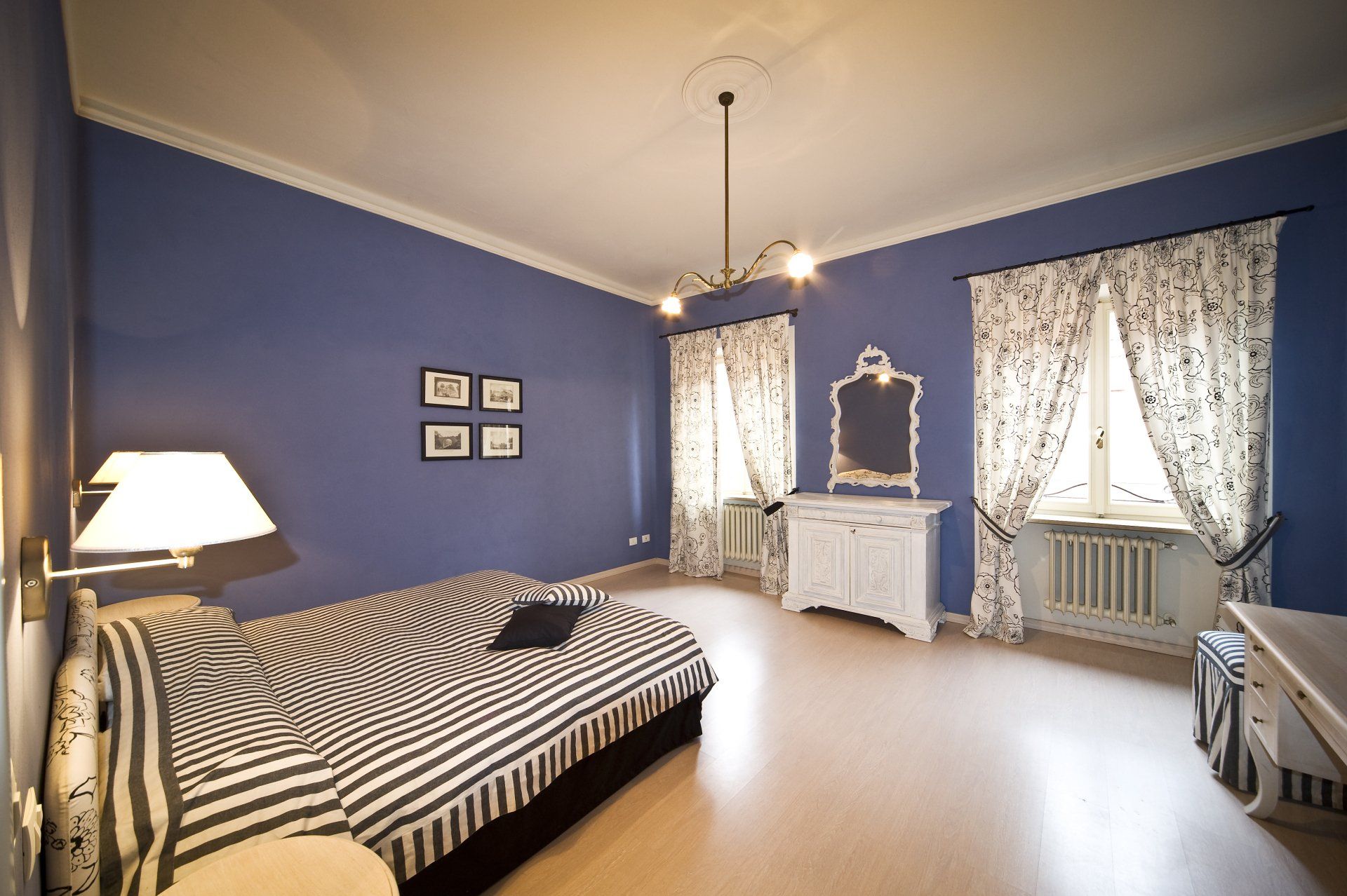 Camera da letto con pareti blu, letto zebrato, tende floreali, cassettiera bianca e lampada a soffitto.