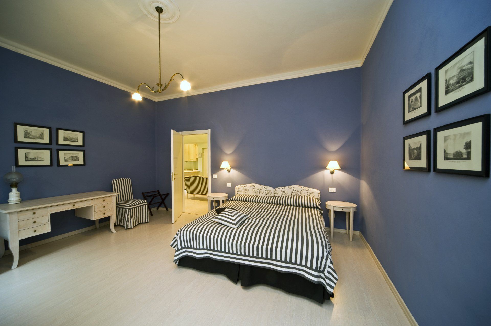 Camera da letto blu con biancheria da letto a righe, mobili bianchi e foto incorniciate alle pareti.