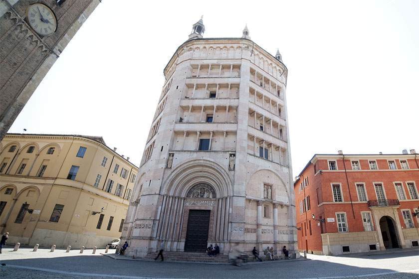 Battistero ottagonale bianco a Parma, Italia. Ingresso con portale ad arco. Edifici che incorniciano la struttura.