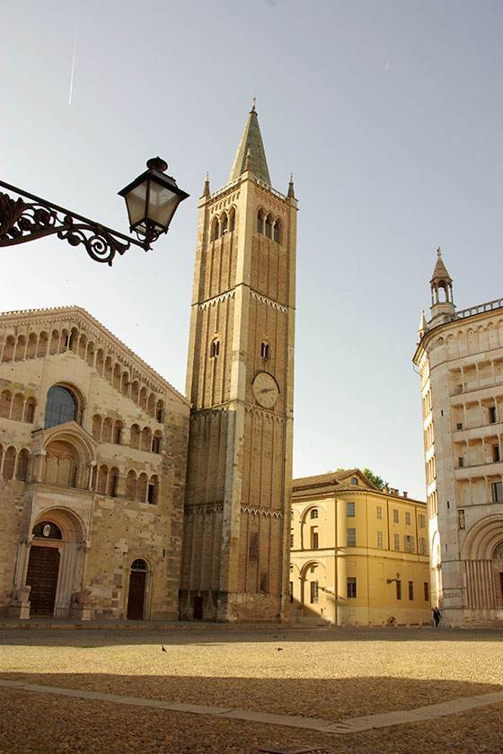 Un'alta cattedrale e una torre dell'orologio a Parma, in Italia, con uno sfondo di cielo azzurro e limpido.
