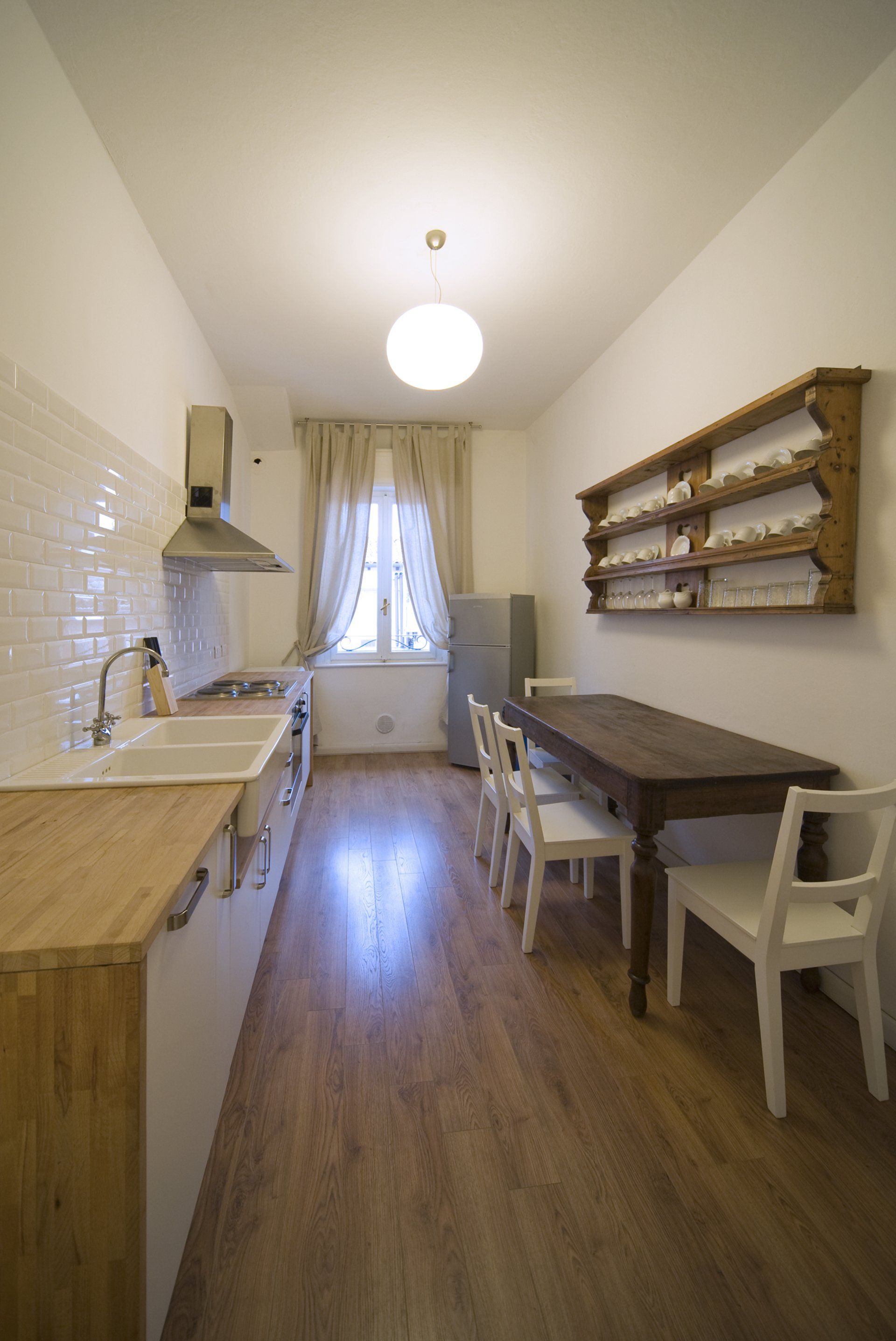 Piccola cucina con mobili bianchi, ripiani in legno e un tavolo da pranzo con quattro sedie bianche.
