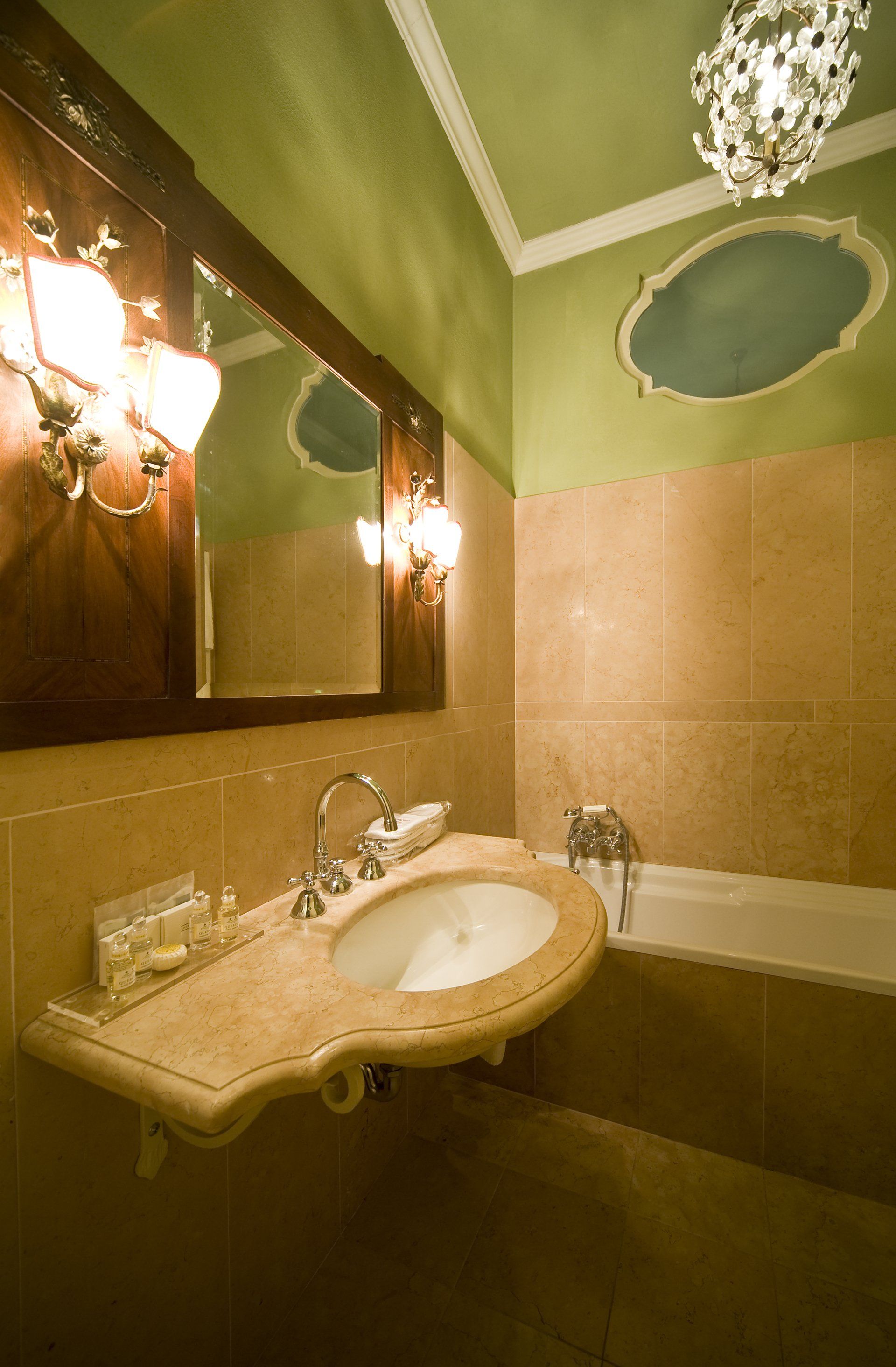 Elegante bagno con pareti verdi, specchio decorato, lavandino in marmo e vasca da bagno.