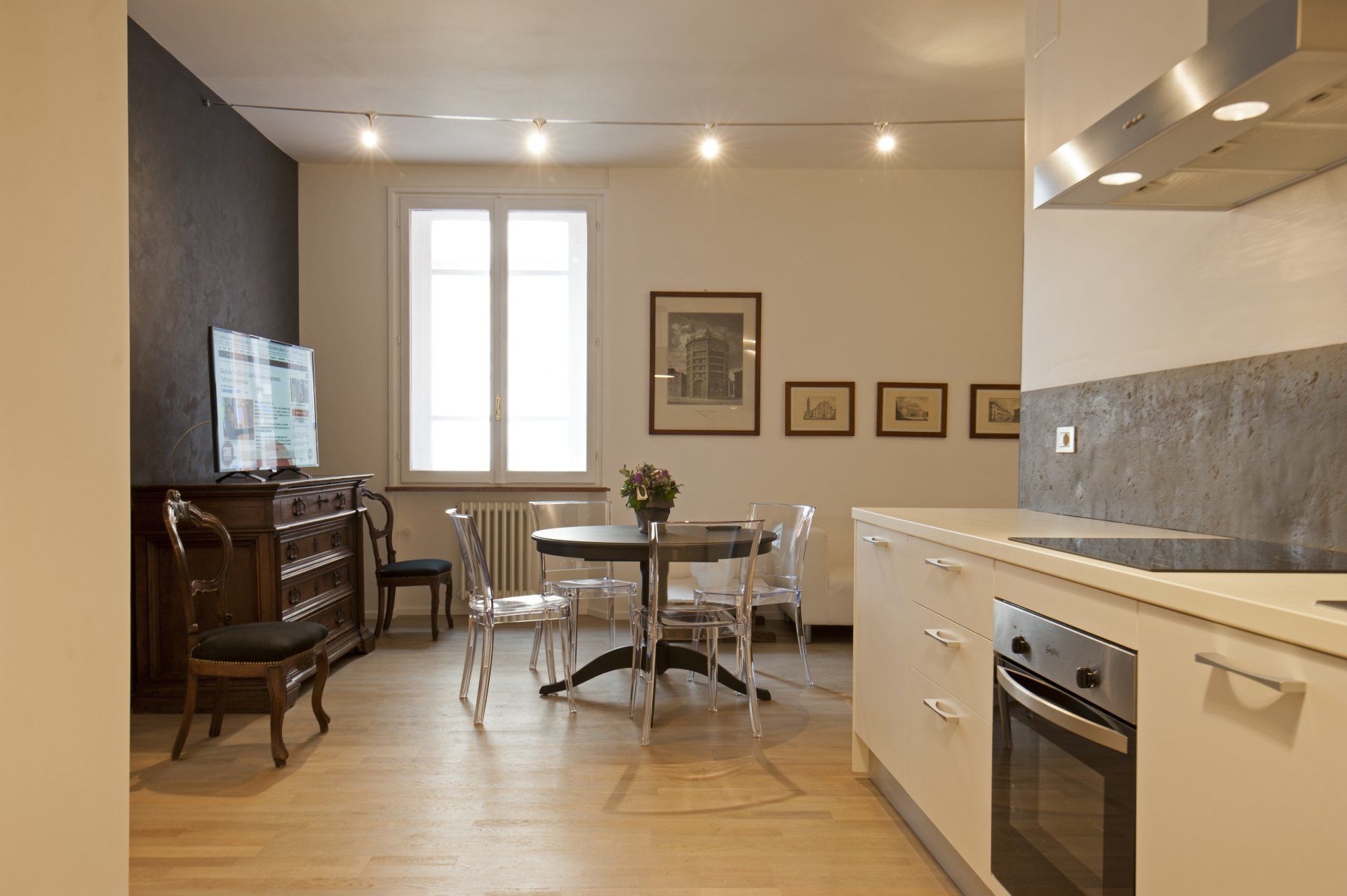 Spazio abitativo open space con cucina, zona pranzo e soggiorno, pavimento in legno chiaro, pareti bianche, stile moderno.