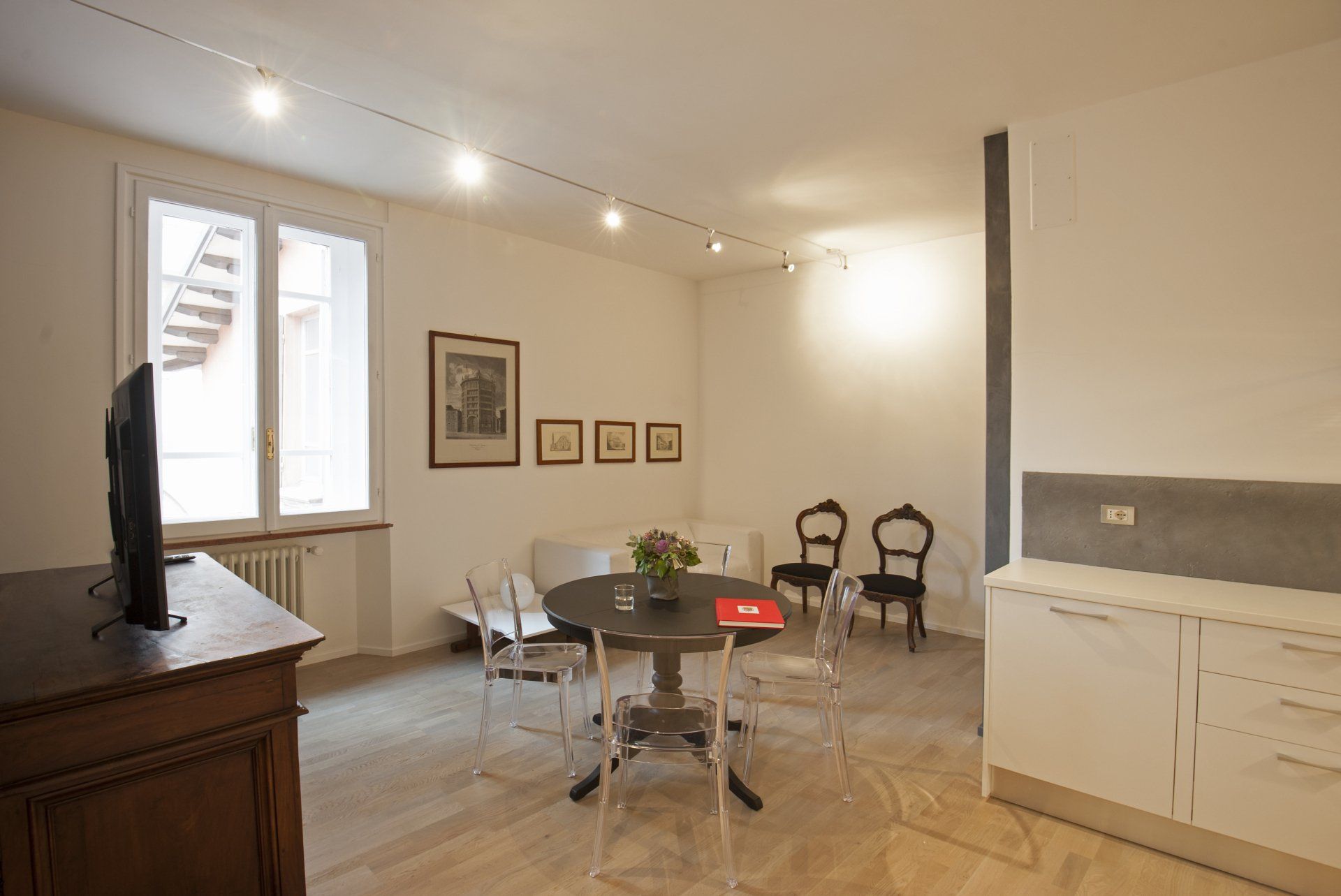 Soggiorno con tavolo rotondo, sedie, divanetto, opere d'arte, finestra e mobili bianchi.