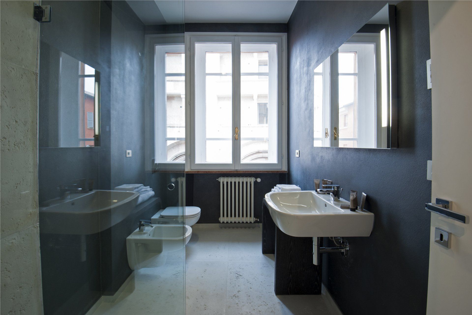 Bagno moderno con pareti blu scuro, sanitari bianchi e una finestra.
