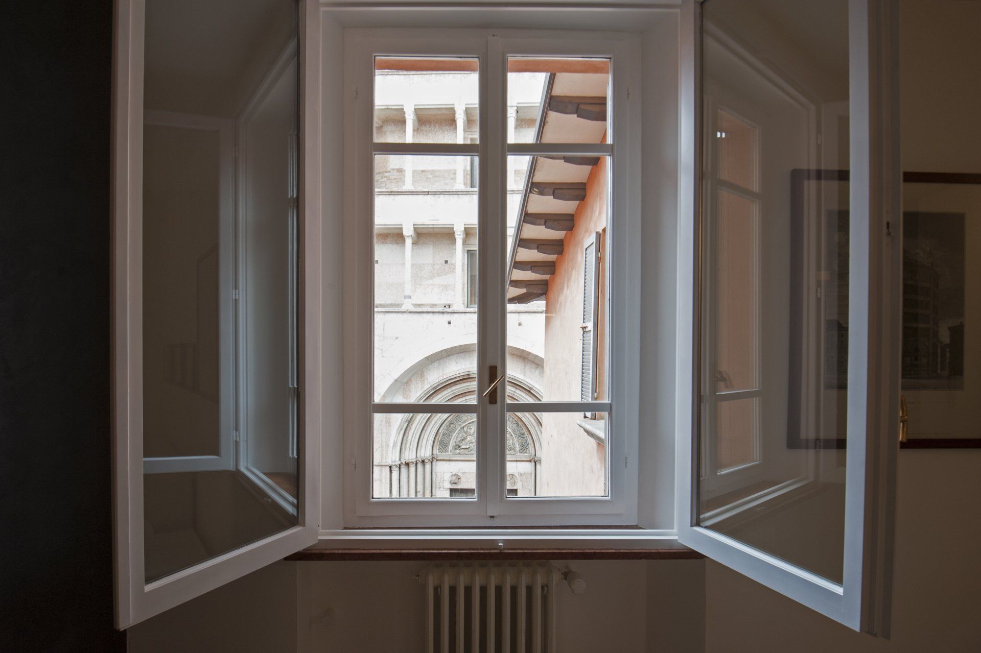 Le finestre bianche aperte rivelano una vista architettonica esterna, probabilmente un cortile.
