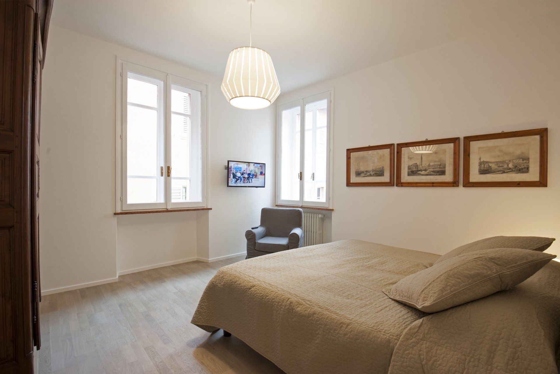 Camera da letto con letto, sedia, due finestre, stampe artistiche e lampada a sospensione.