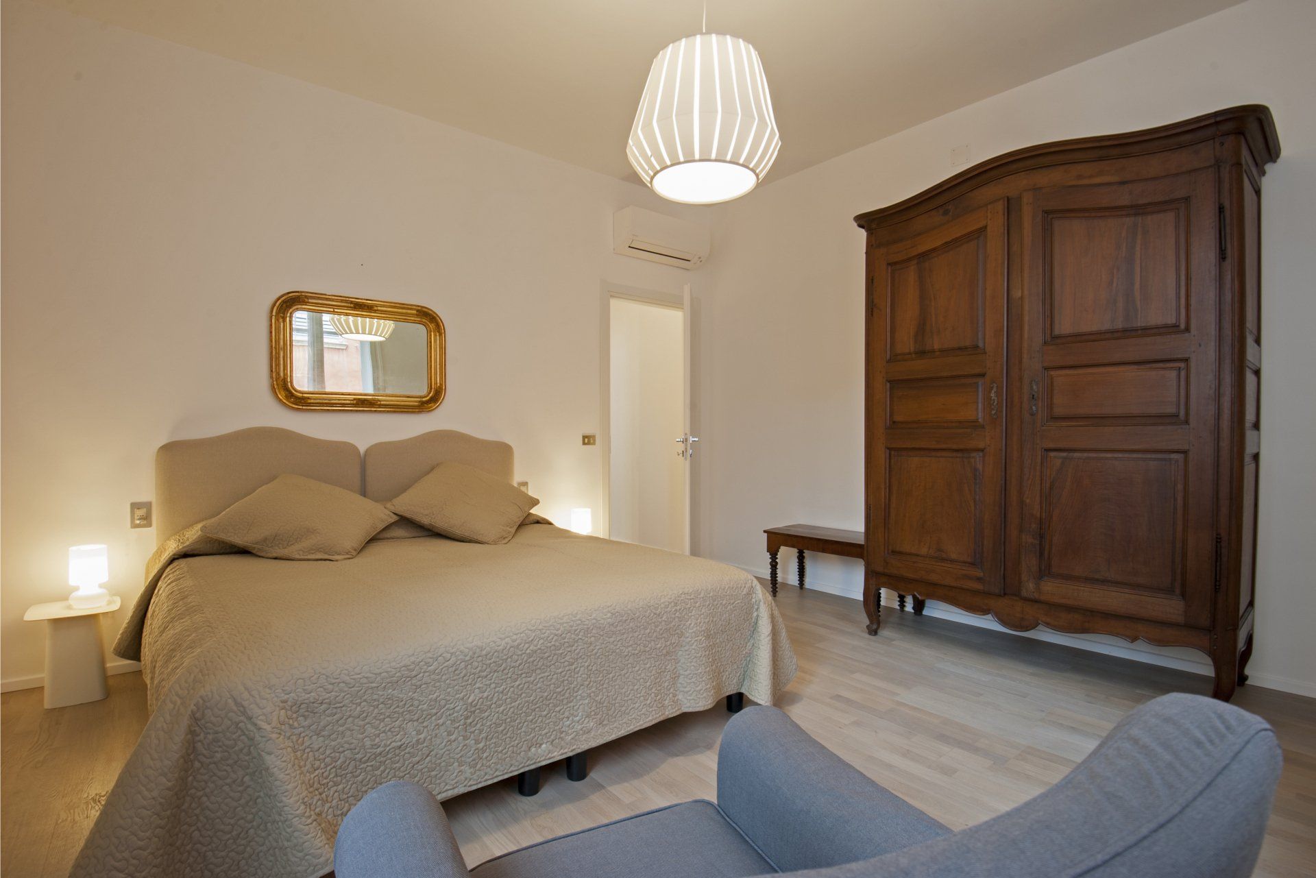 Camera da letto con letto matrimoniale, armadio in legno e sedia di colore chiaro; pavimenti in legno chiaro.