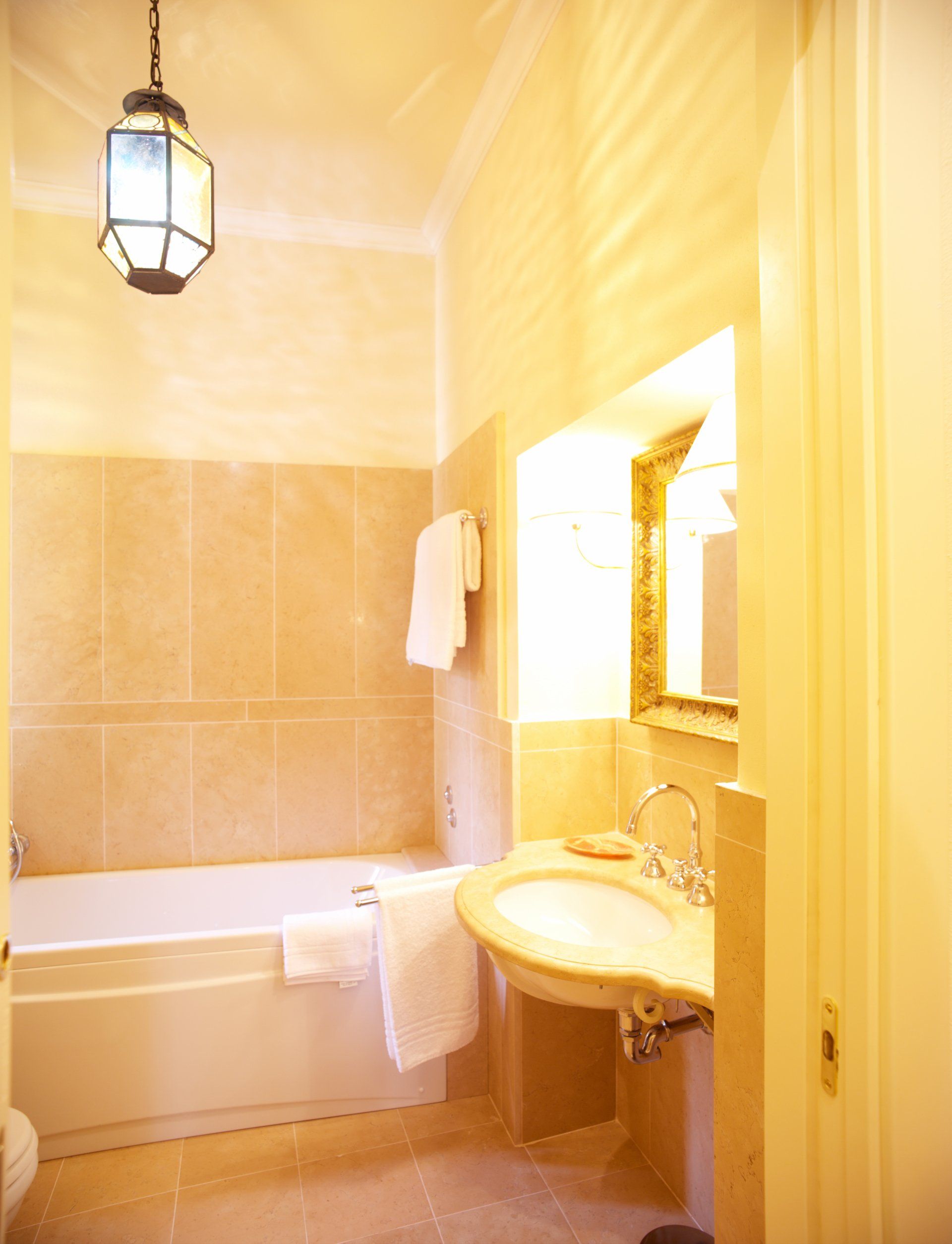 Bagno con pareti piastrellate beige, vasca da bagno, lavandino e lanterna appesa.