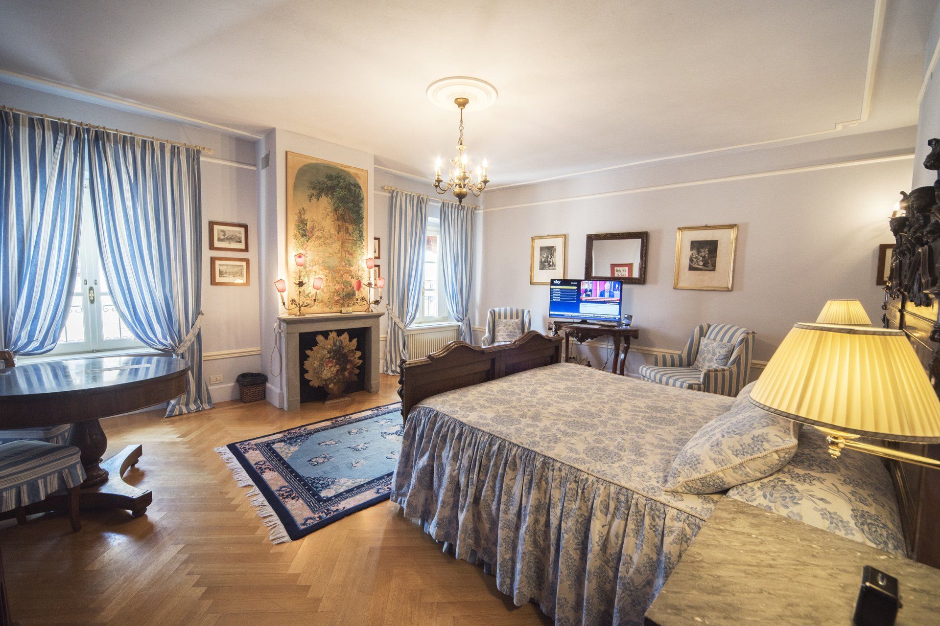 Elegante camera da letto con decorazioni blu e bianche, pavimenti in legno, camino e un letto.
