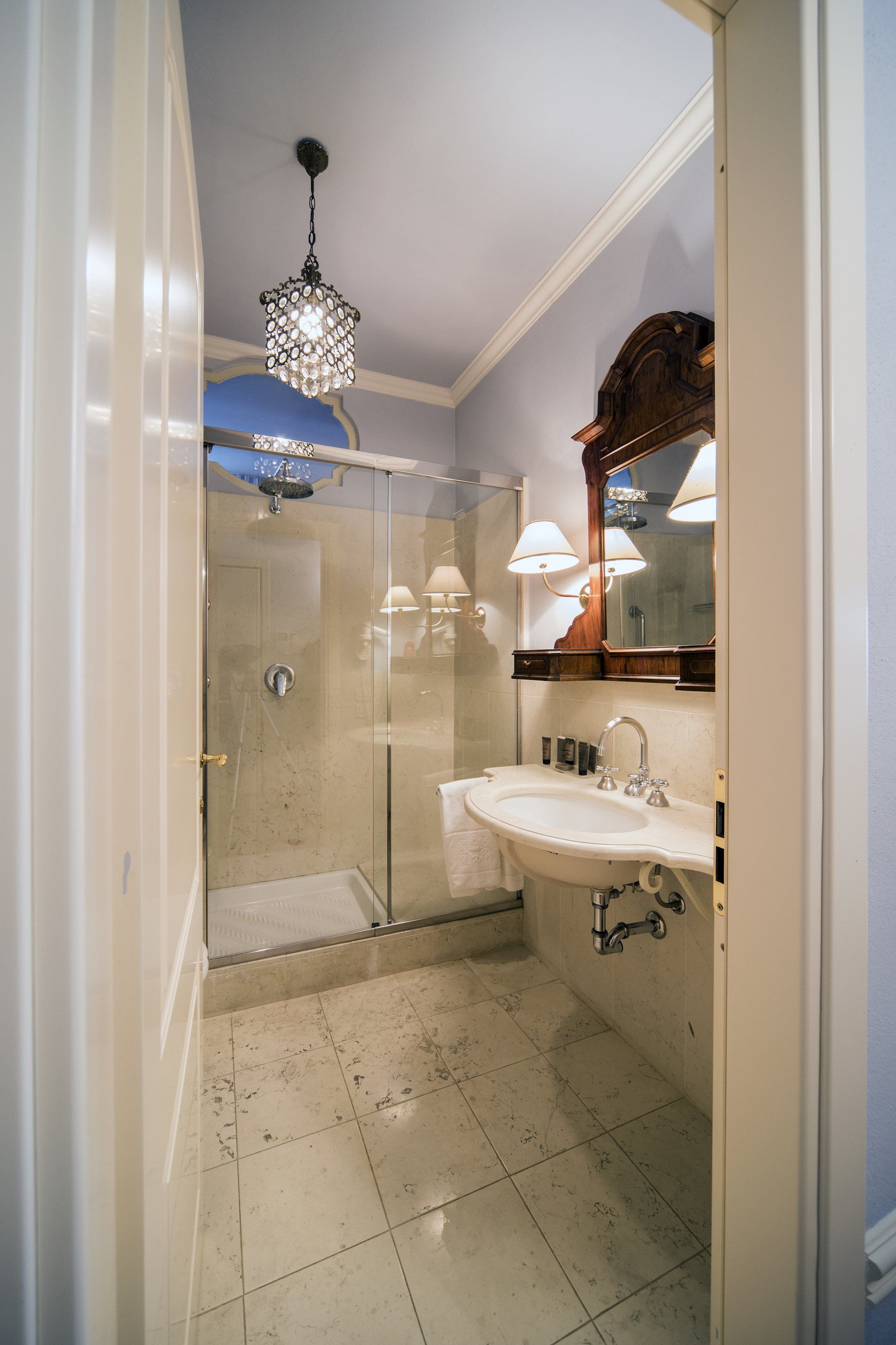 Bagno stretto con doccia, lavandino e specchio decorato. Pareti azzurre, pavimento in piastrelle a fantasia.
