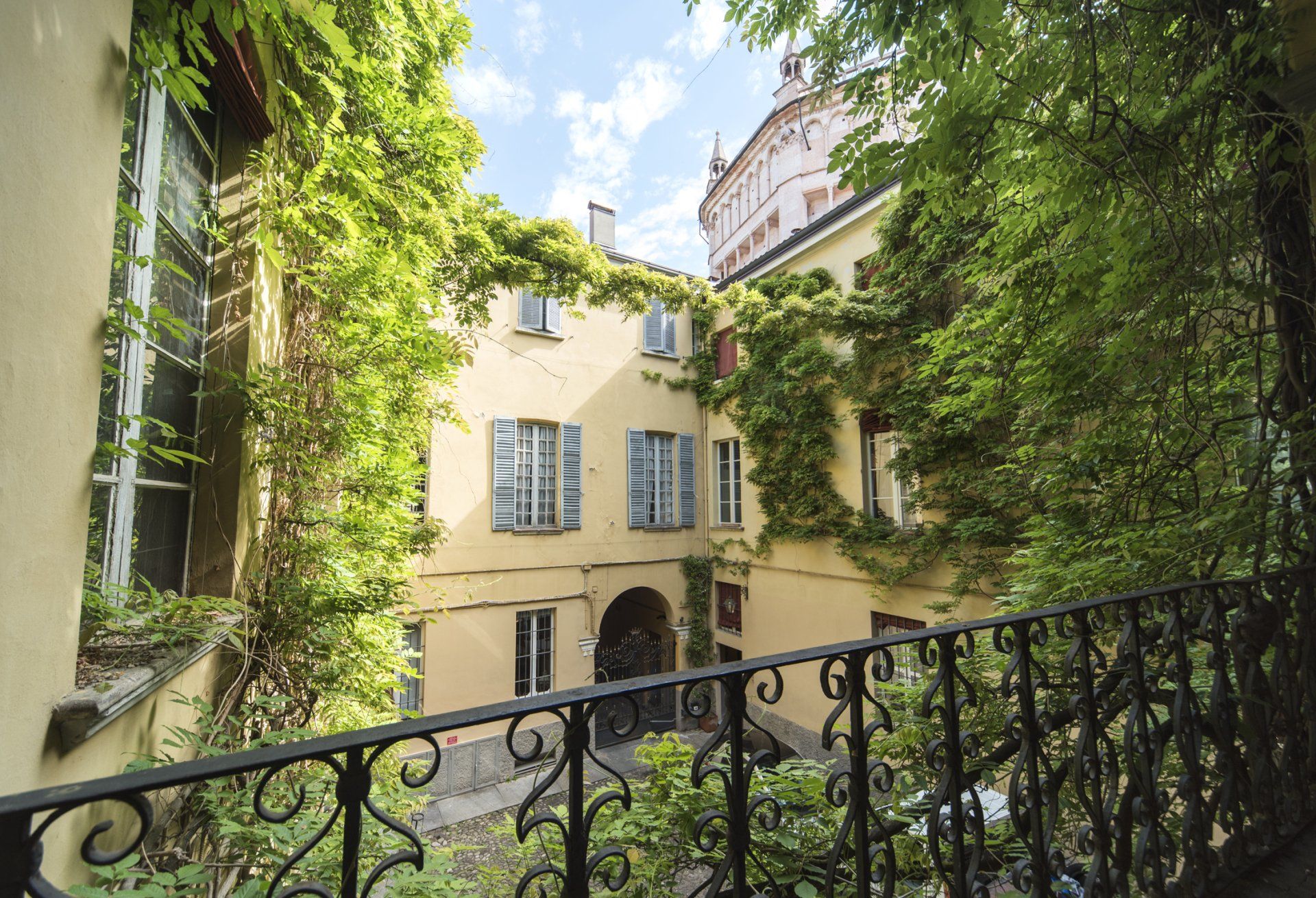 Cortile con edificio ricoperto di edera e ringhiera in ferro battuto.