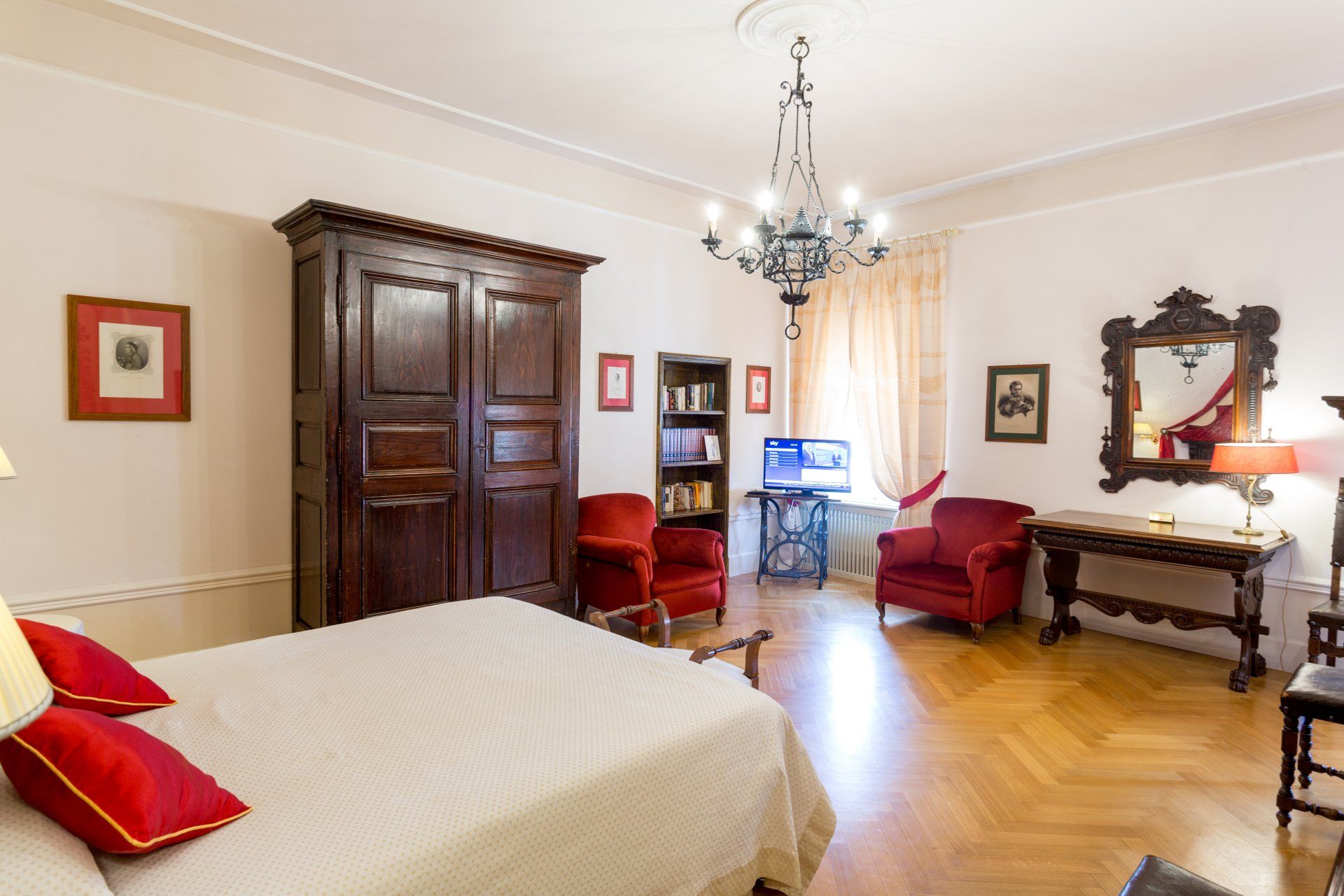 Camera da letto con pavimenti in legno, grande armadio in legno, poltrone rosse e lampadario.
