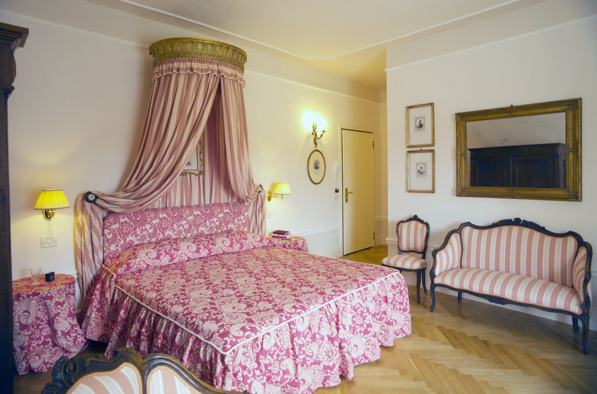 Camera da letto rosa e bianca con letto a baldacchino, mobili decorati e tessuti a fantasia; pavimenti in parquet.