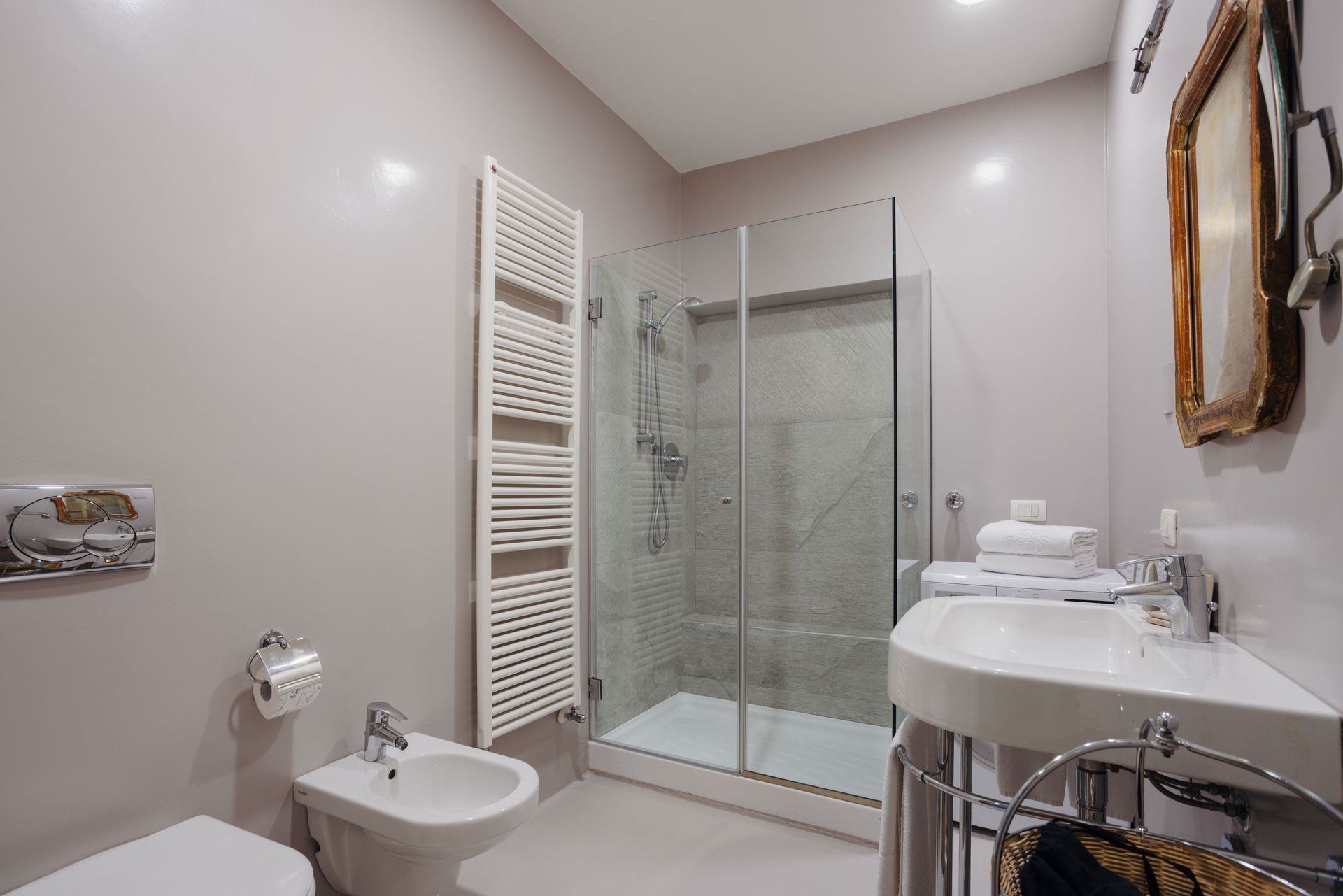 Bagno con doccia, WC, lavandino e portasciugamani. Pareti e pavimento grigio chiaro.
