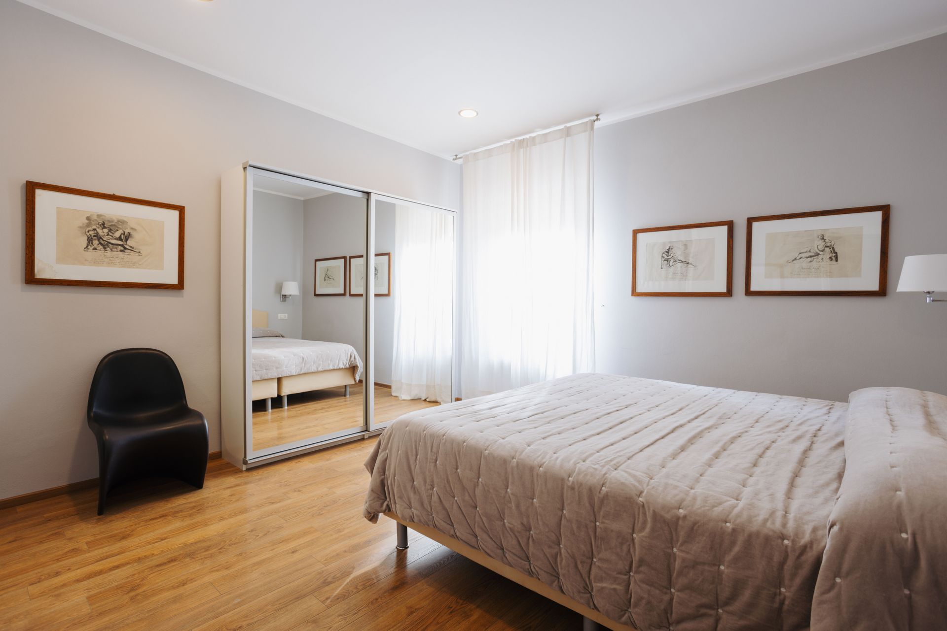 Camera da letto con letto matrimoniale, armadio a specchio, pavimento in legno, pareti grigie e opere d'arte incorniciate.