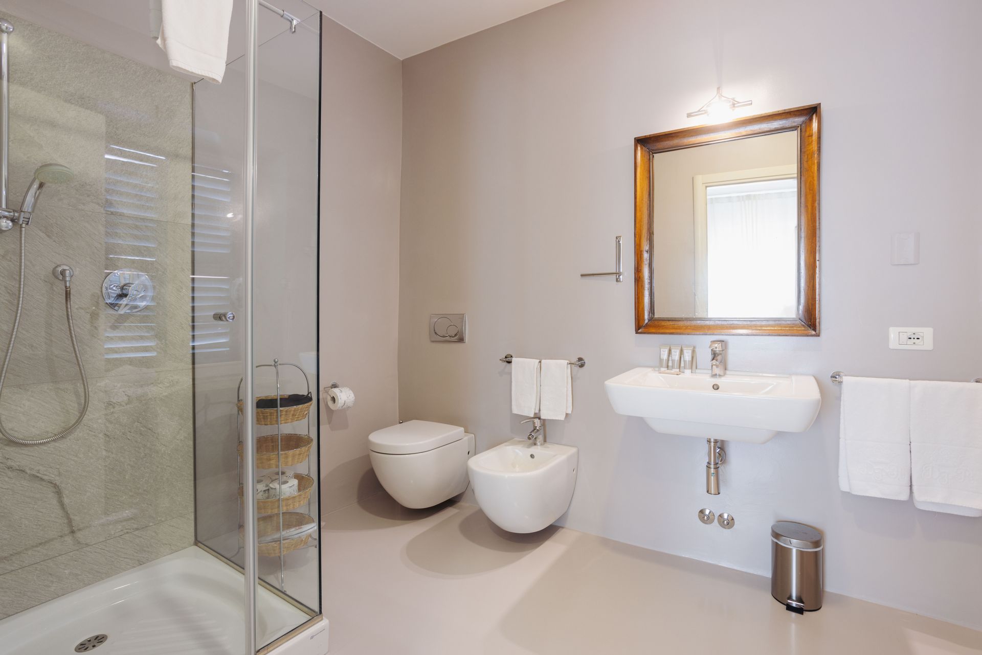 Bagno moderno con doccia in vetro, WC, bidet, lavandino, specchio e asciugamani.