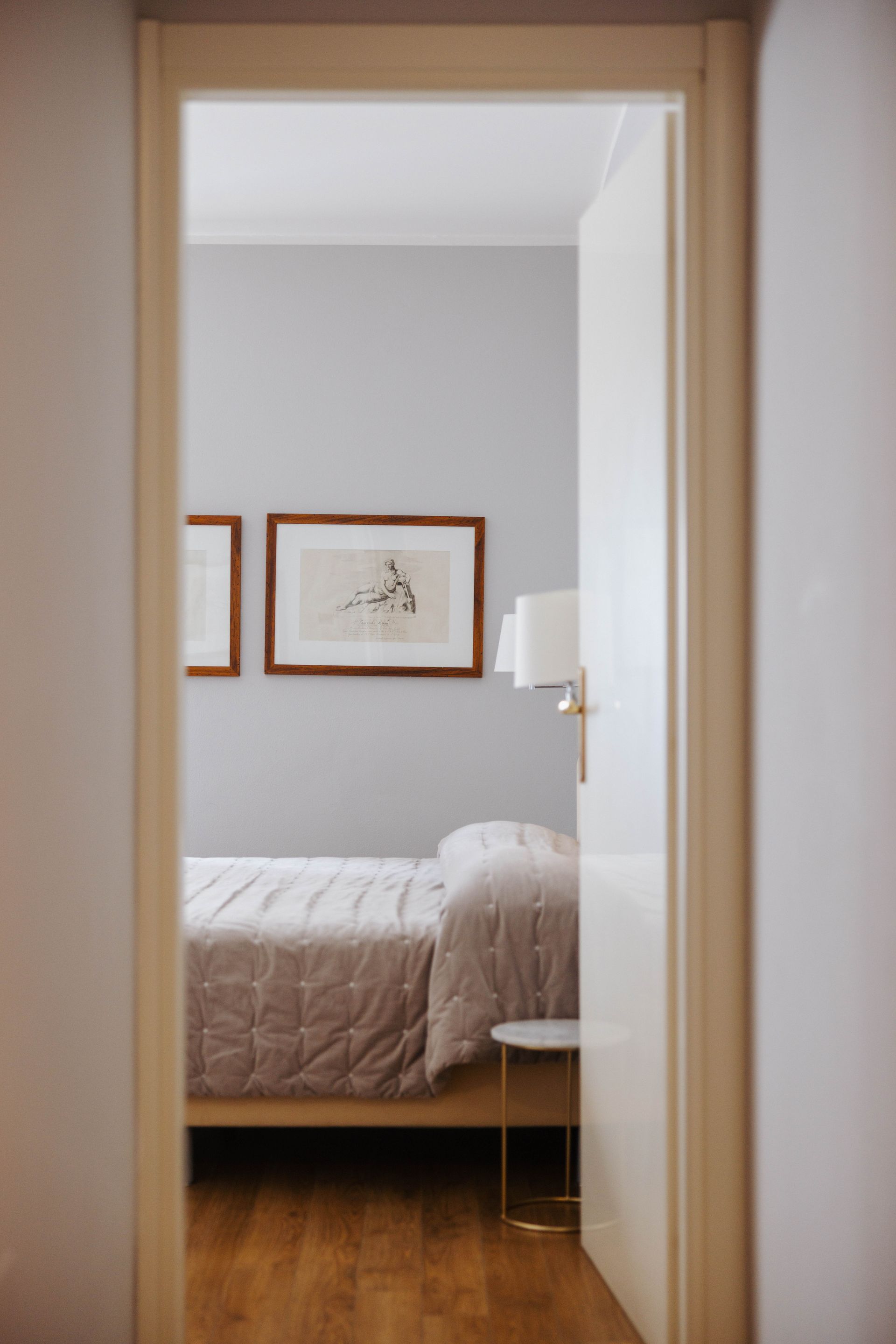 Camera da letto vista dalla porta, letto con trapunta, opere d'arte, pareti grigio chiaro.