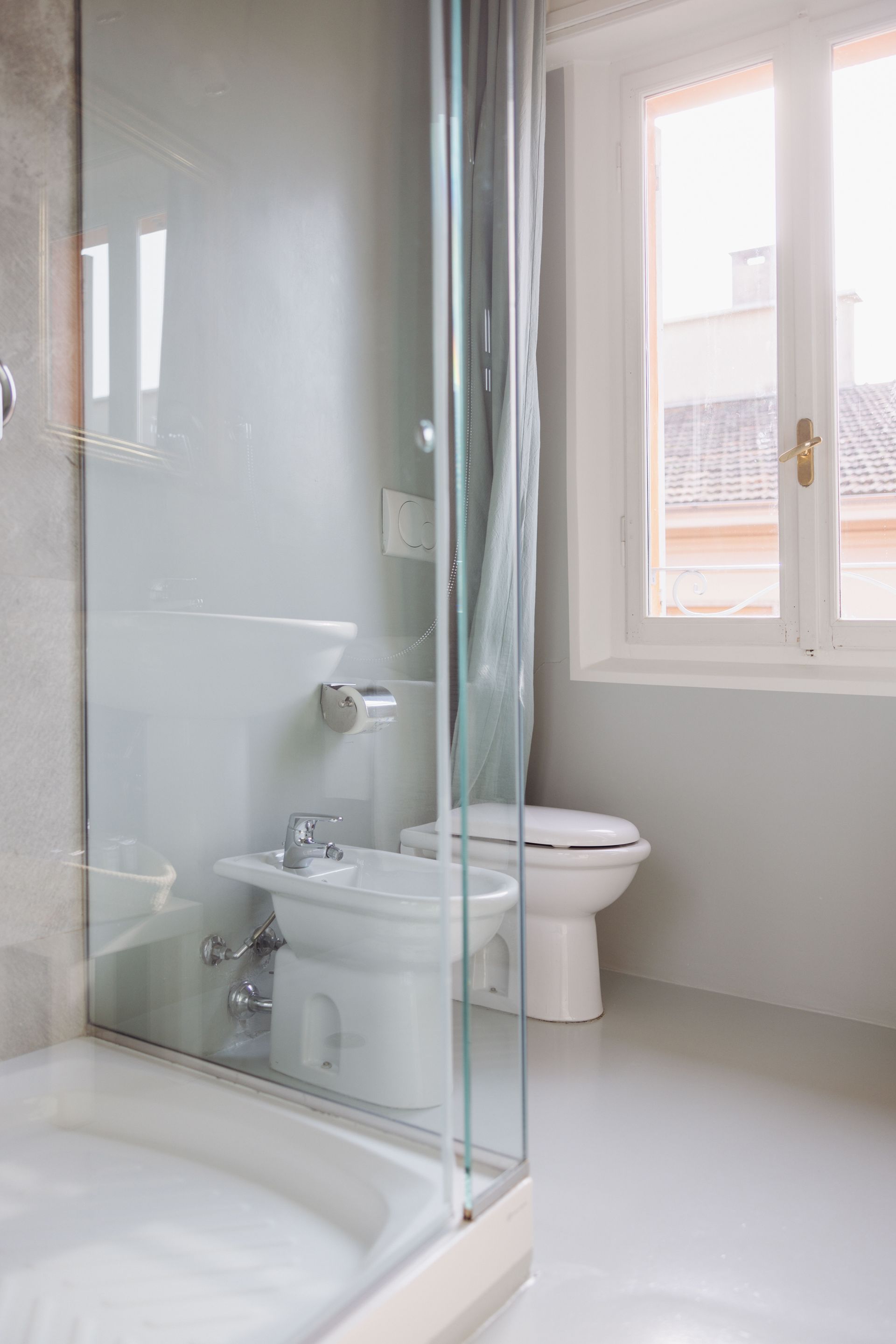 Bagno con doccia, WC e bidet. Porta doccia in vetro. Finestra con luce naturale. Pareti grigie, sanitari bianchi.