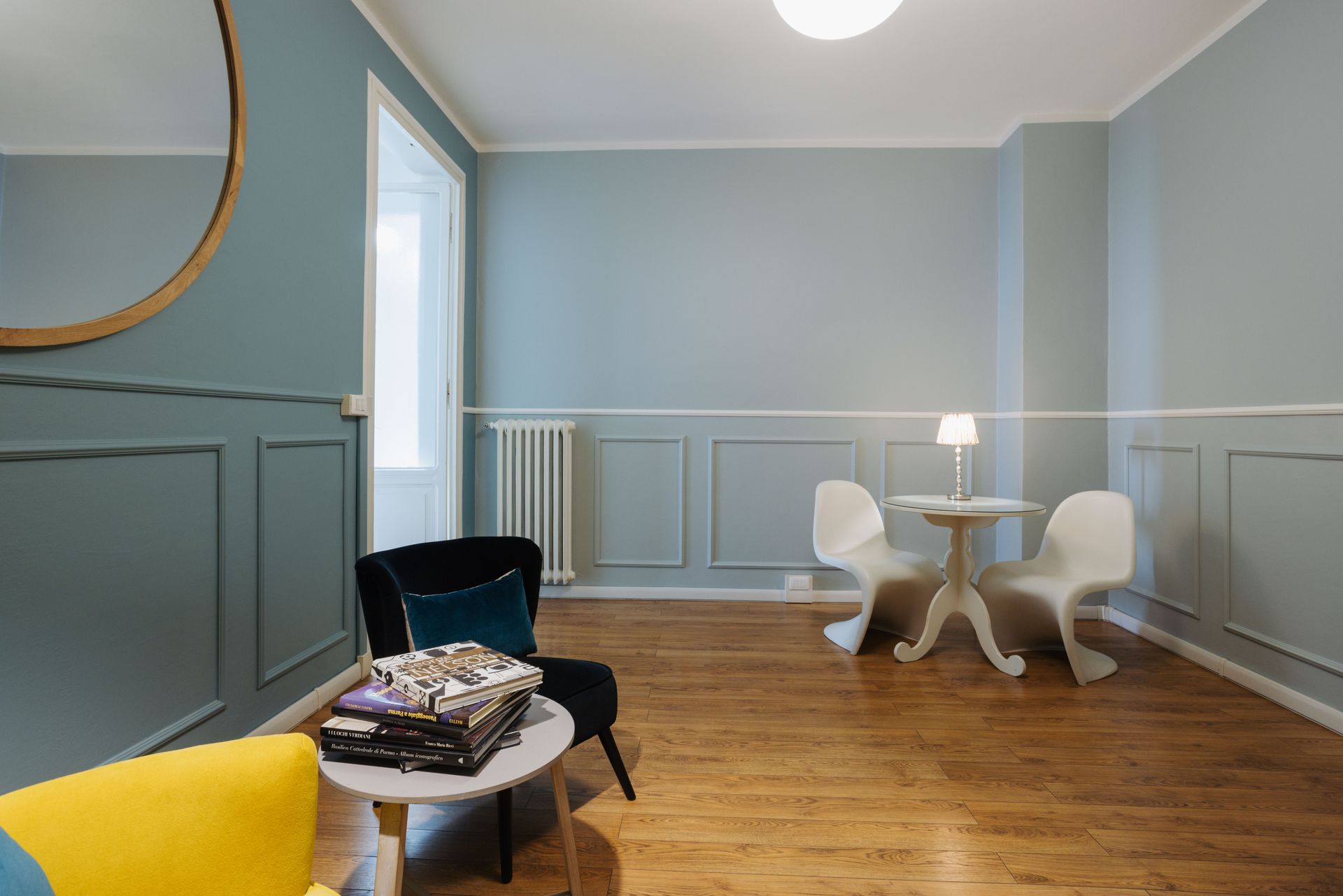Una stanza con pareti blu, finiture bianche, pavimento in legno, due sedie e un tavolino.