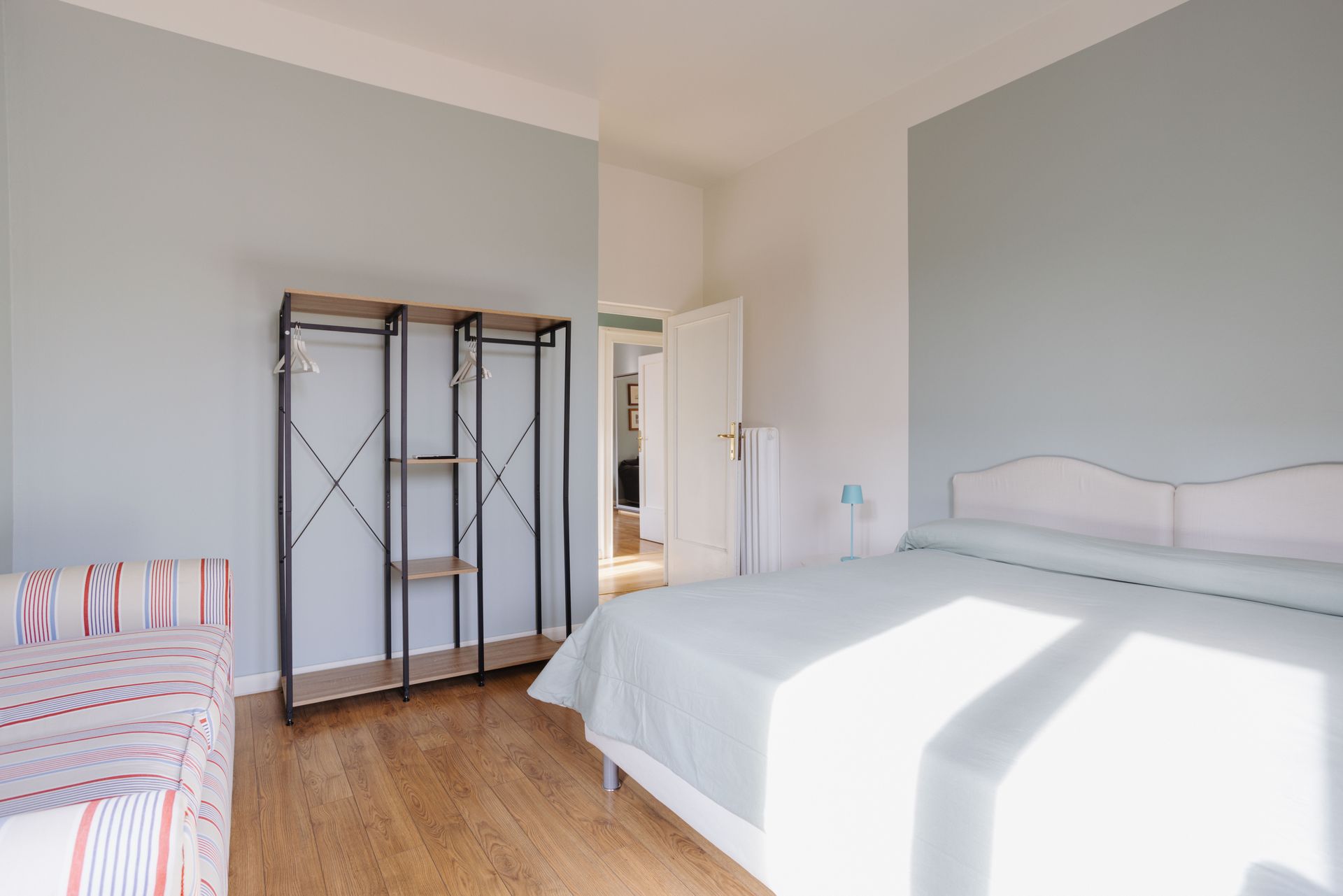 Camera da letto con letto, armadio e divano a righe; pareti azzurre e pavimento in legno.