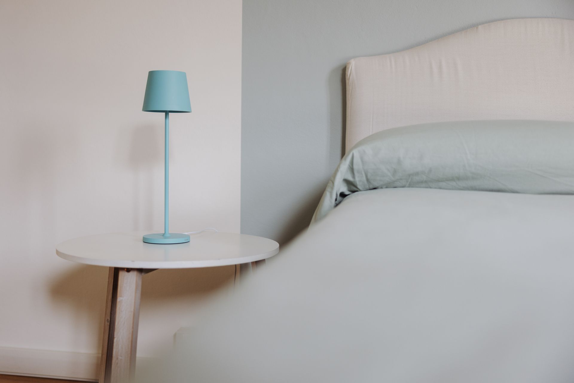 Lampada azzurra su un comodino bianco accanto a un letto con lenzuola azzurre.