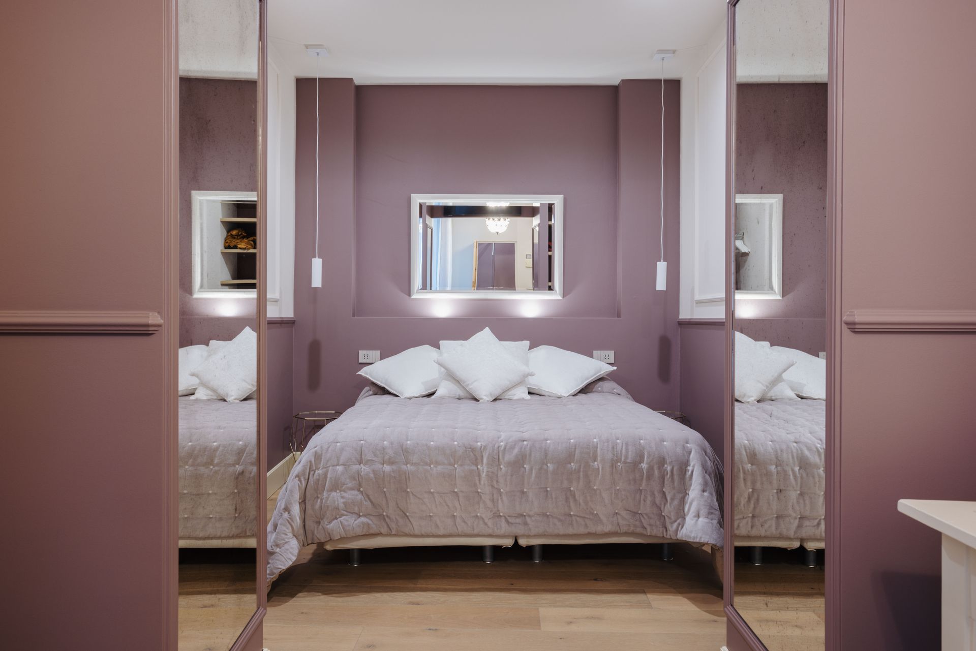 Camera da letto con pareti viola e ante dell'armadio a specchio, letto con cuscini bianchi e luci.