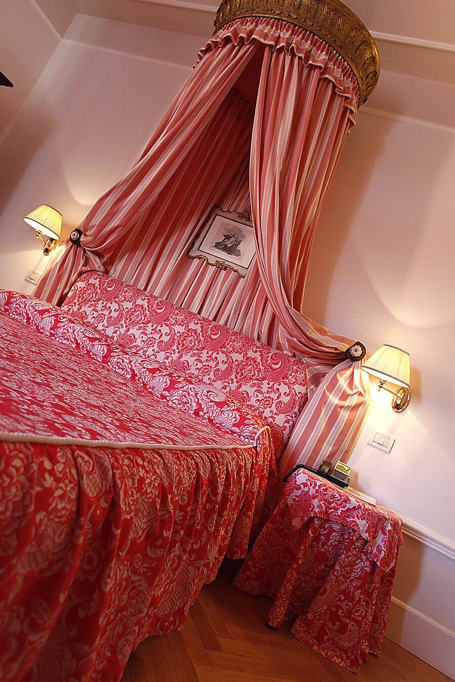 Letto a baldacchino rosso in una stanza con comodino coordinato. Dettagli dorati, design ricercato.