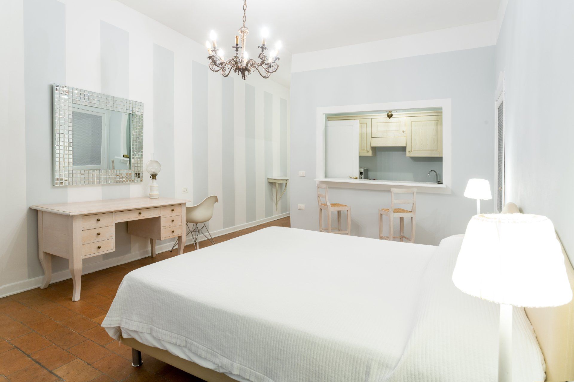 Camera da letto con letto, scrivania, cucina a vista e parete a strisce azzurre e bianche.