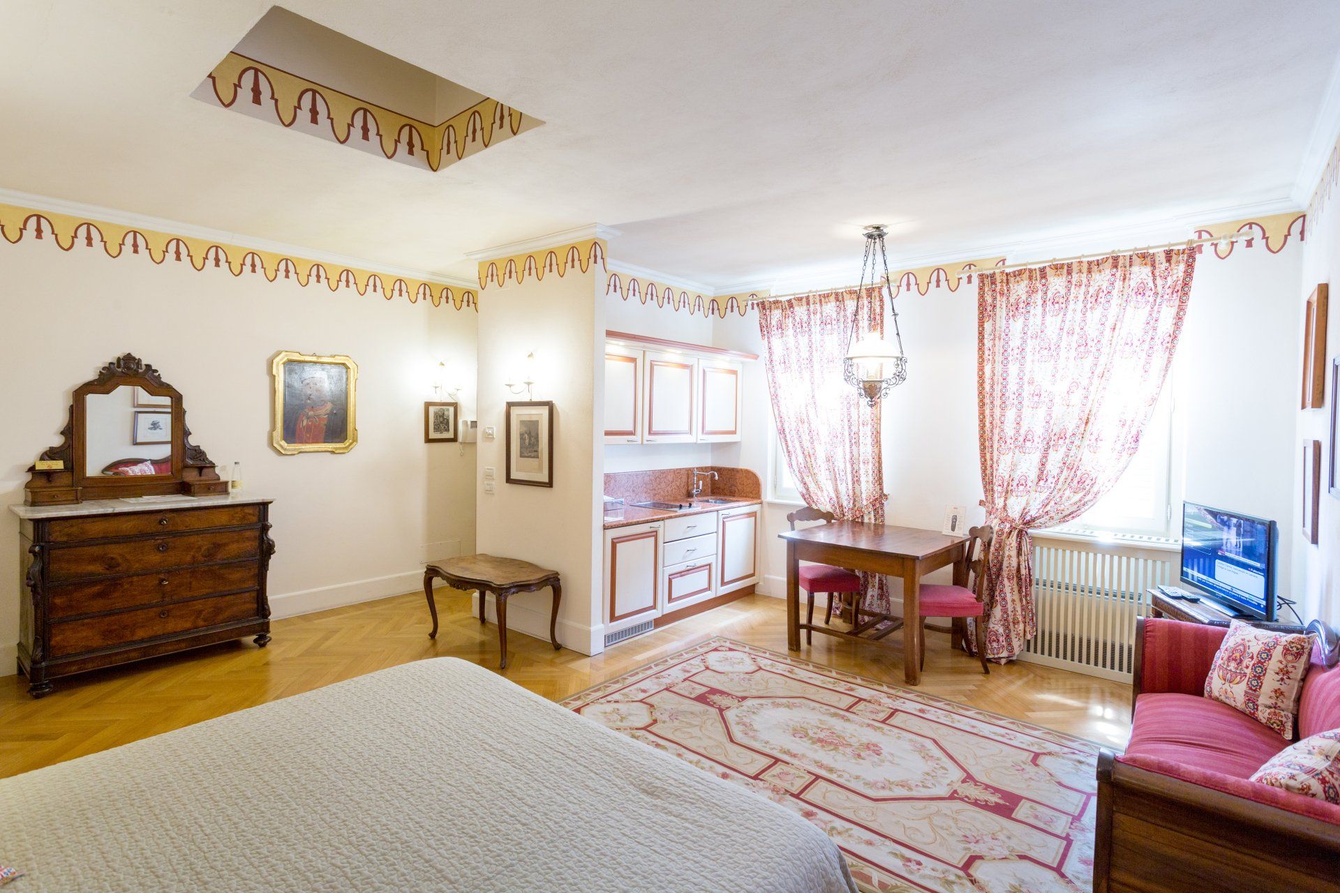 Accogliente appartamento con dettagli rossi, dotato di letto, divano, cucina e zona pranzo; luminoso, in stile classico.