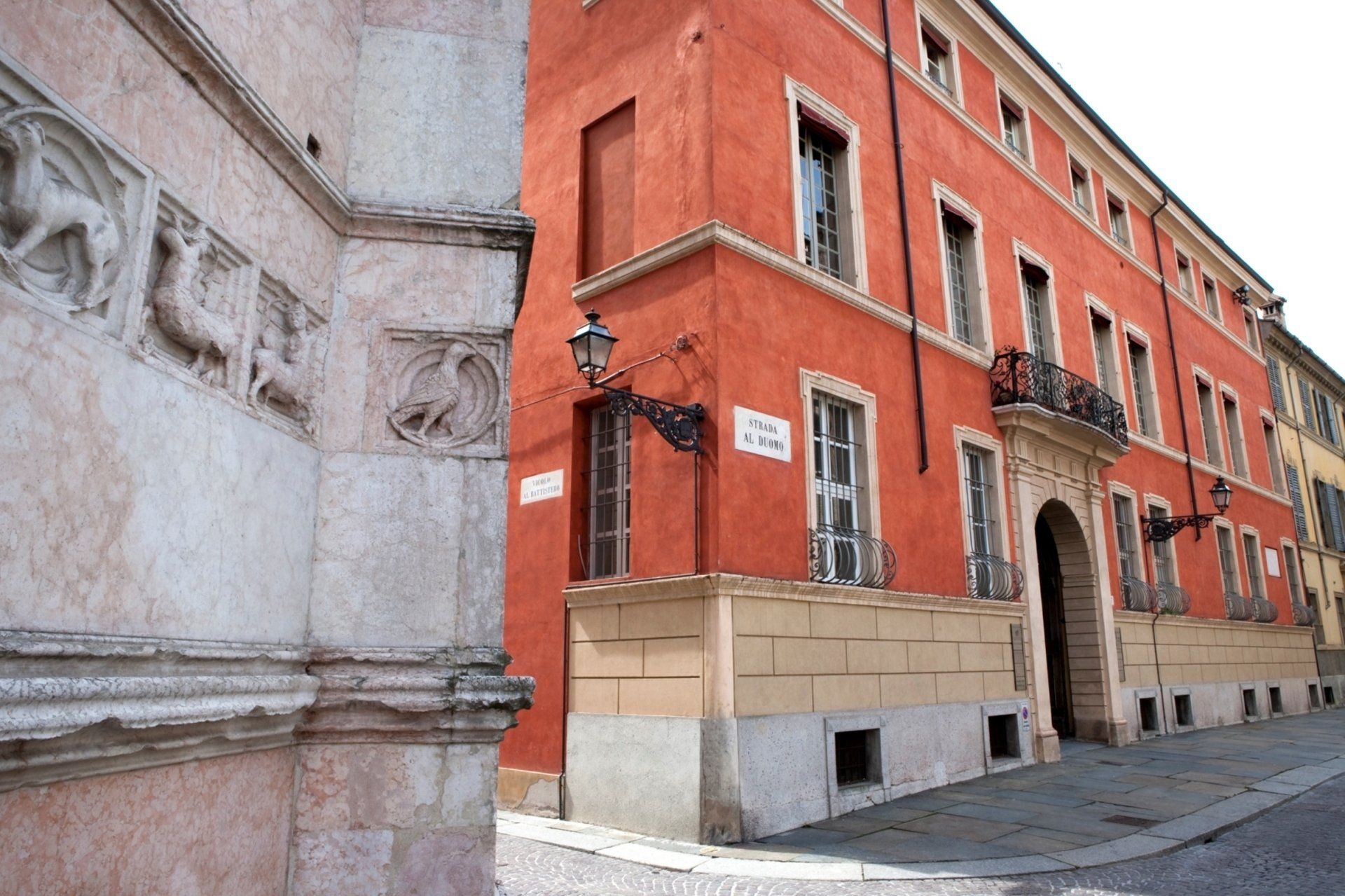 Edificio rosso con un ingresso decorativo in un angolo di strada in Italia. Un muro di pietra si trova sul lato sinistro.