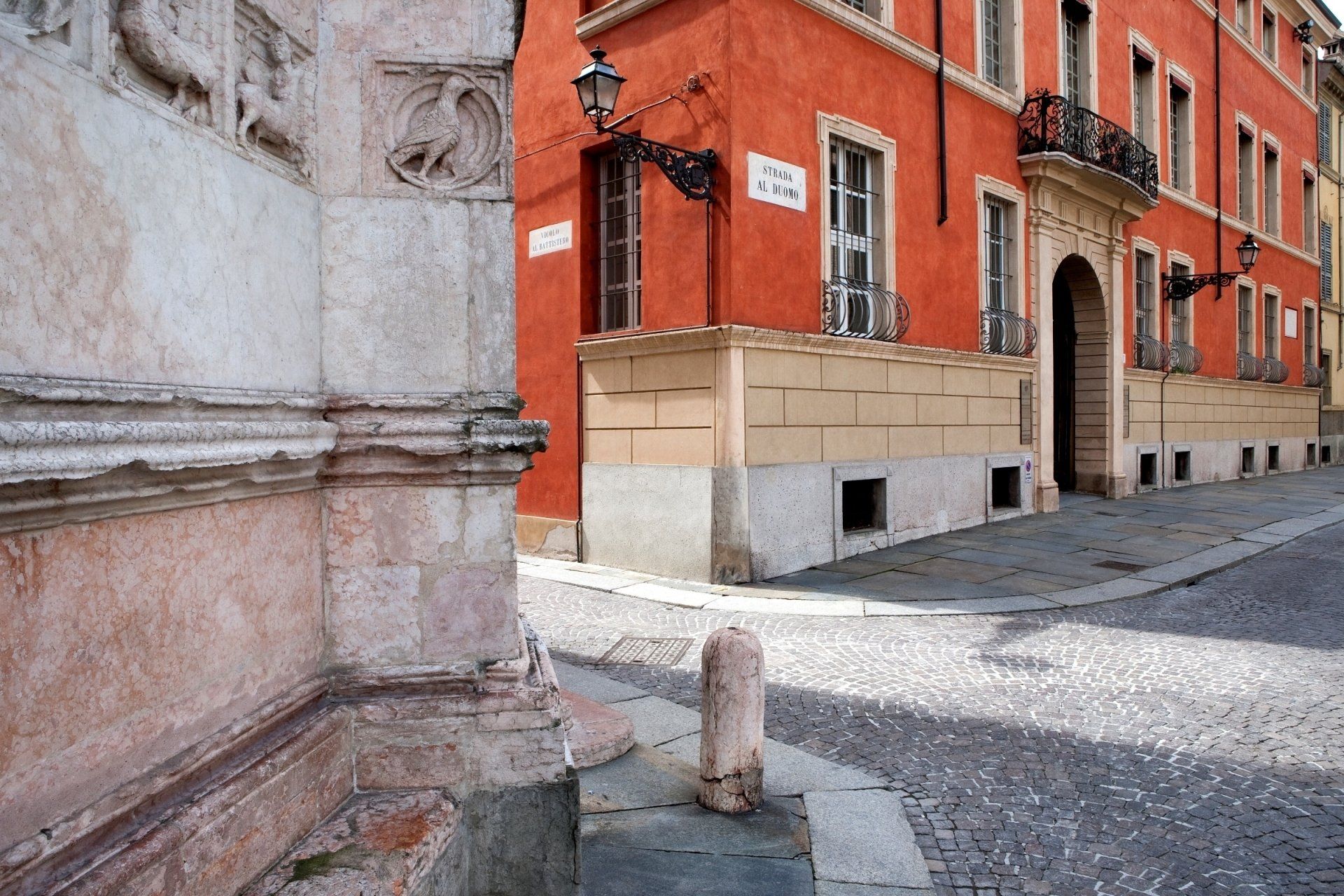 Angolo di edifici in una città italiana. Uno è rosso-arancio, l'altro è in pietra beige, con una strada acciottolata.