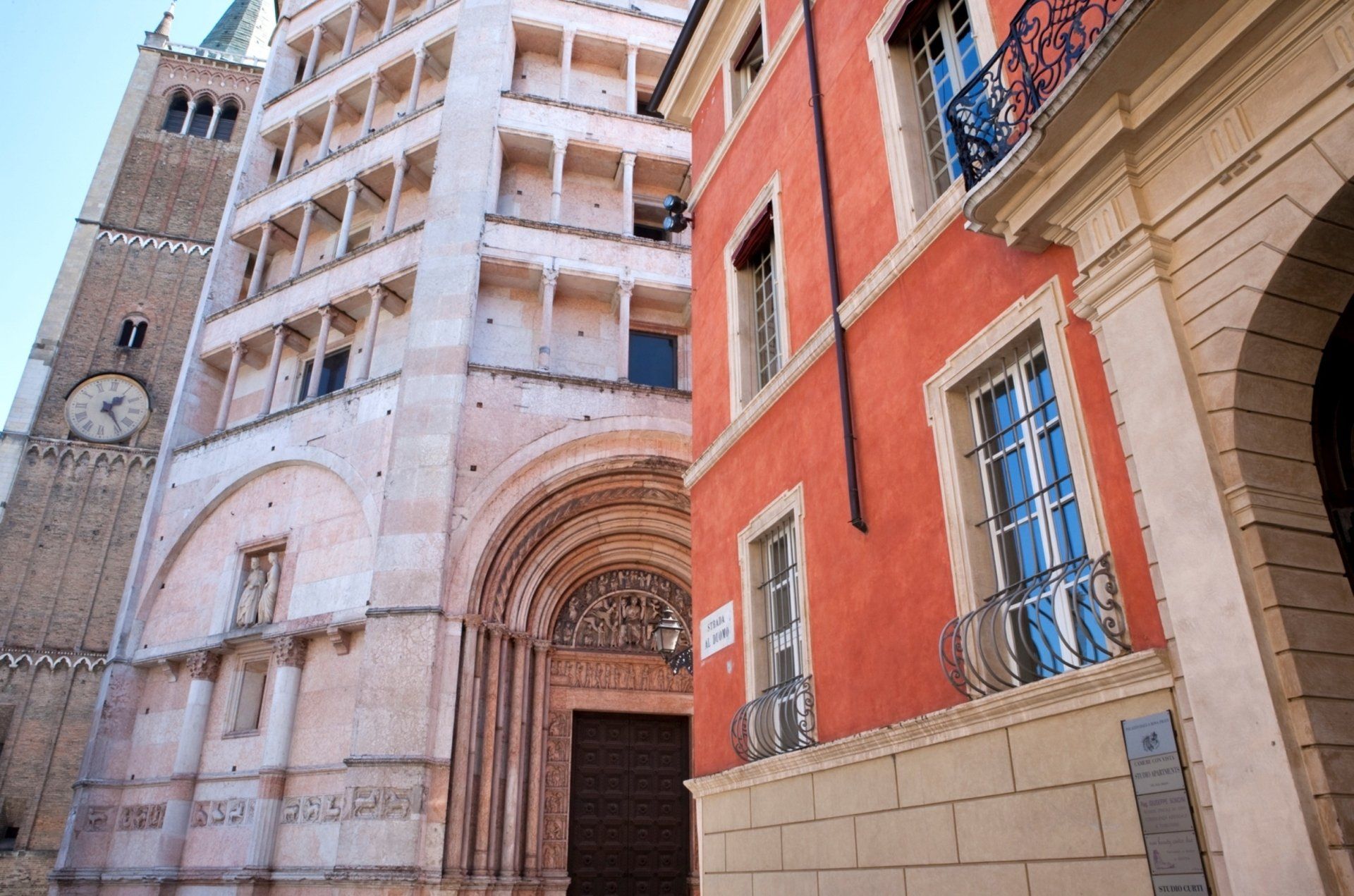 Edifici a Parma, Italia: un'alta cattedrale con una torre dell'orologio e un edificio rosso-arancio.