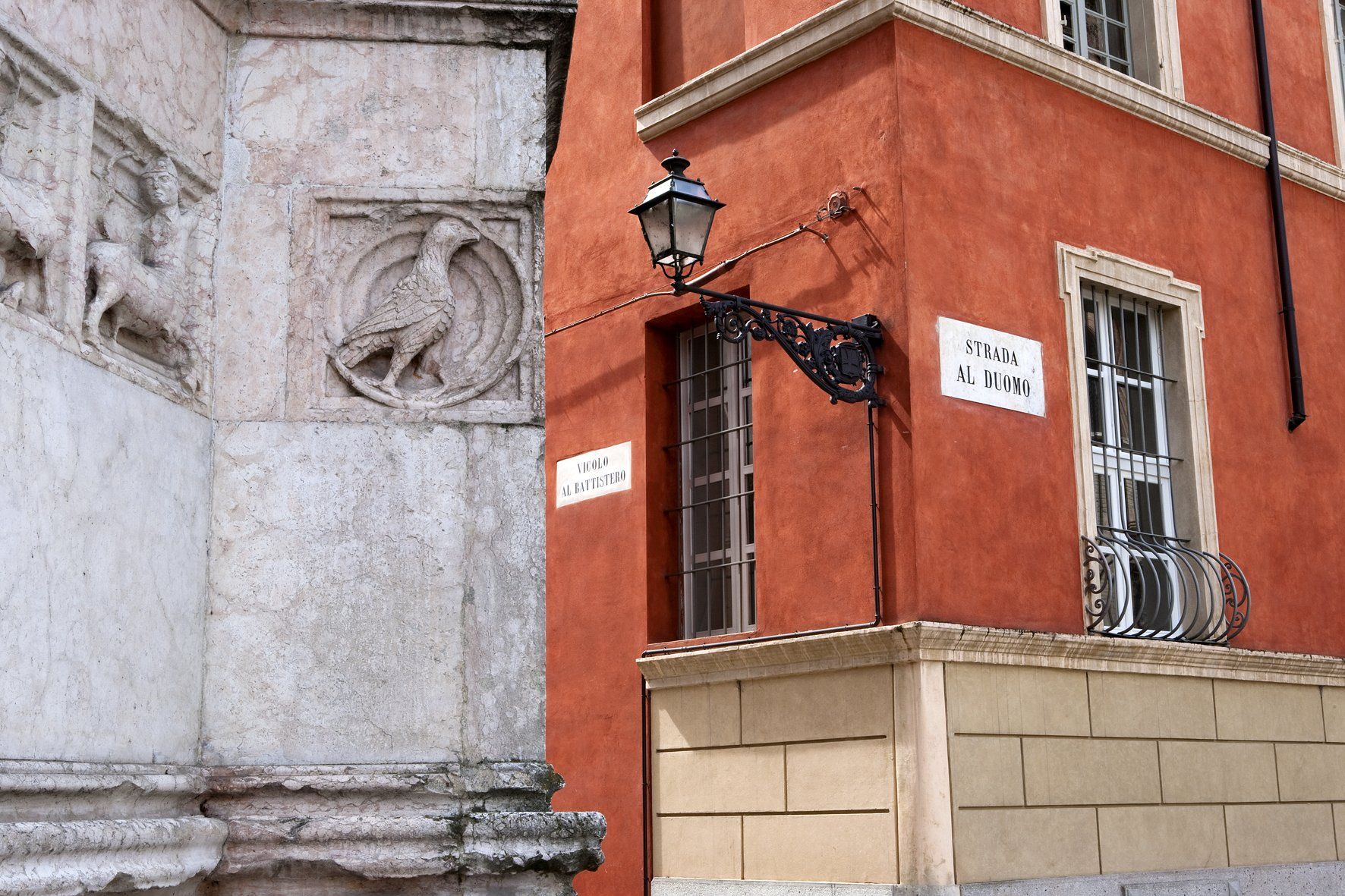 Angolo di edifici; facciata bianca decorata con un rilievo raffigurante un uccello ed esterno in stucco rosso.