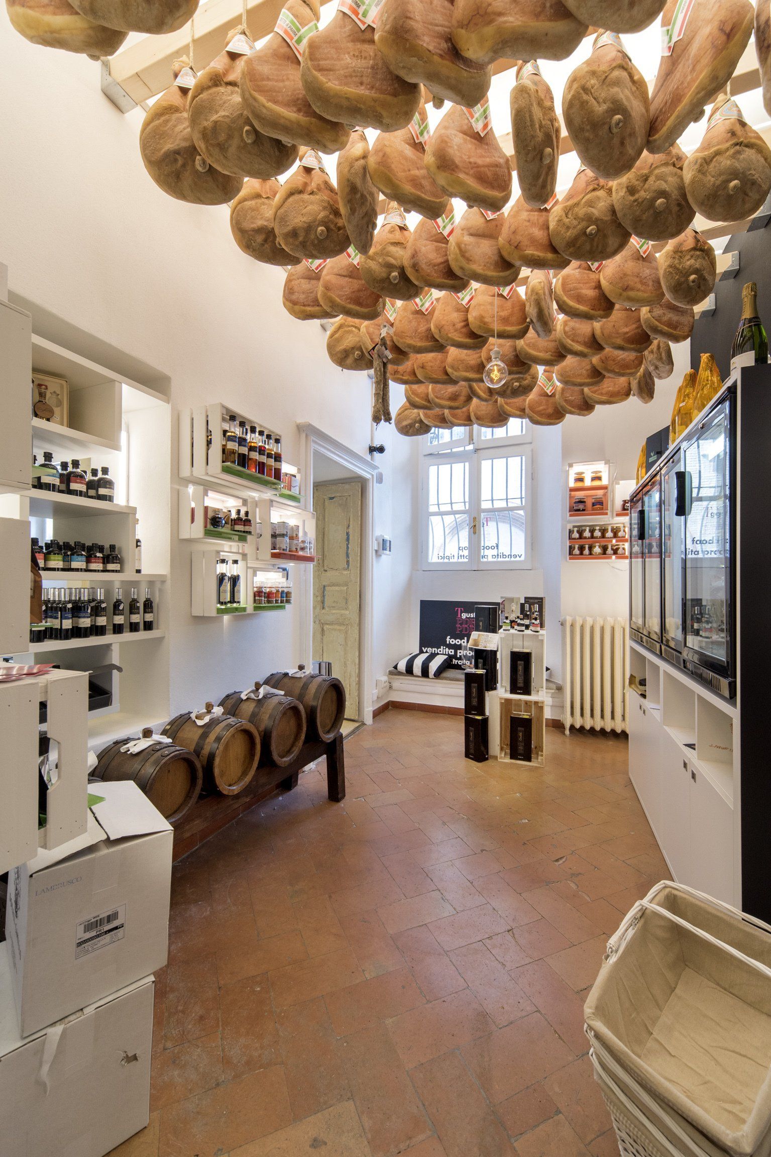 Interno del negozio con salumi appesi, scaffali con prodotti e botti di legno.