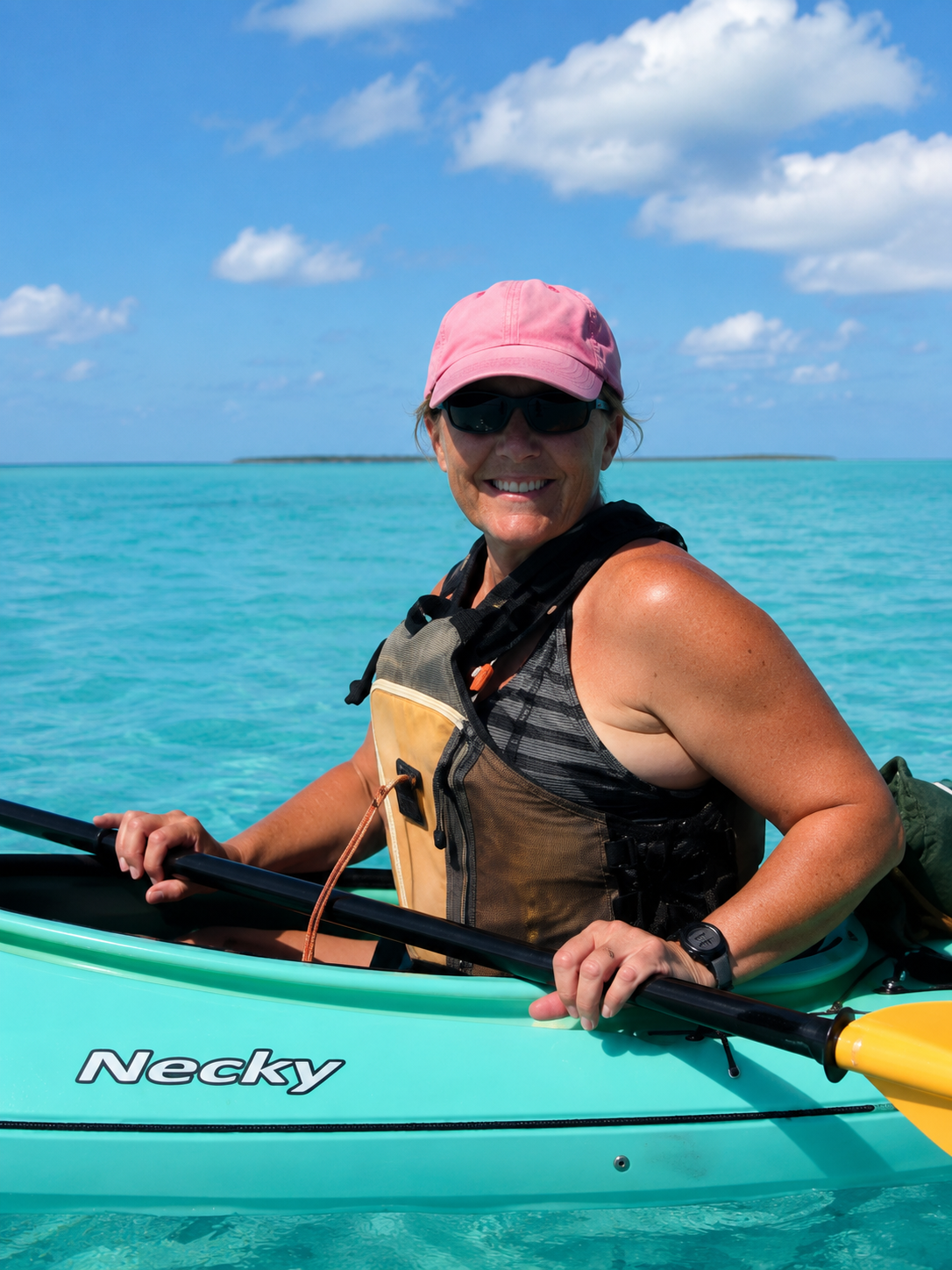 Smiling kayaker in a pink cap on a turquoise kayak in clear blue ocean