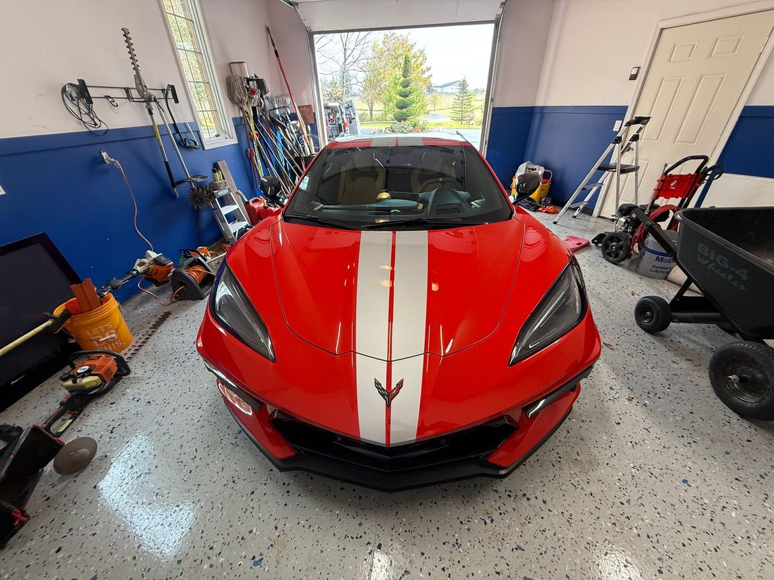 Red sports car with white racing stripes in a garage workshop