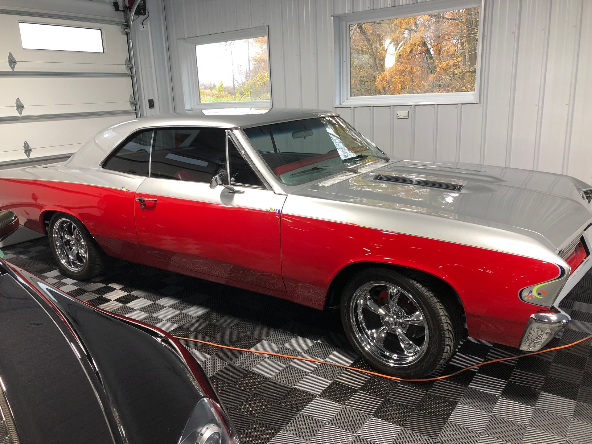 Red and silver classic car parked inside a garage with checkered floor.