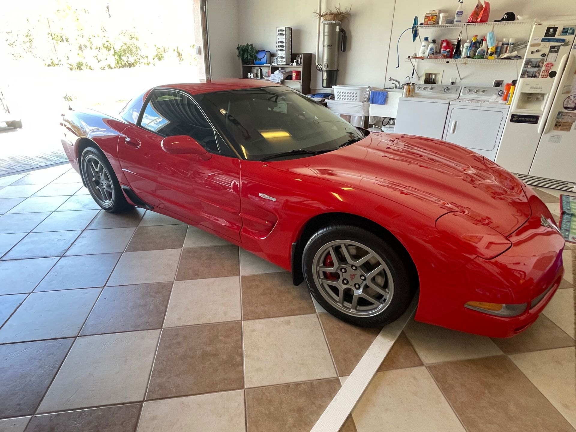 Red sports car parked in a tiled garage with shelves and tools in the background