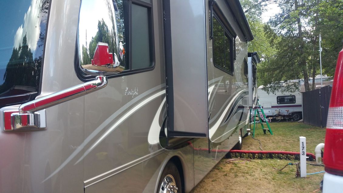 Motorhome parked on grass with slide-out extended, trees and camping gear nearby