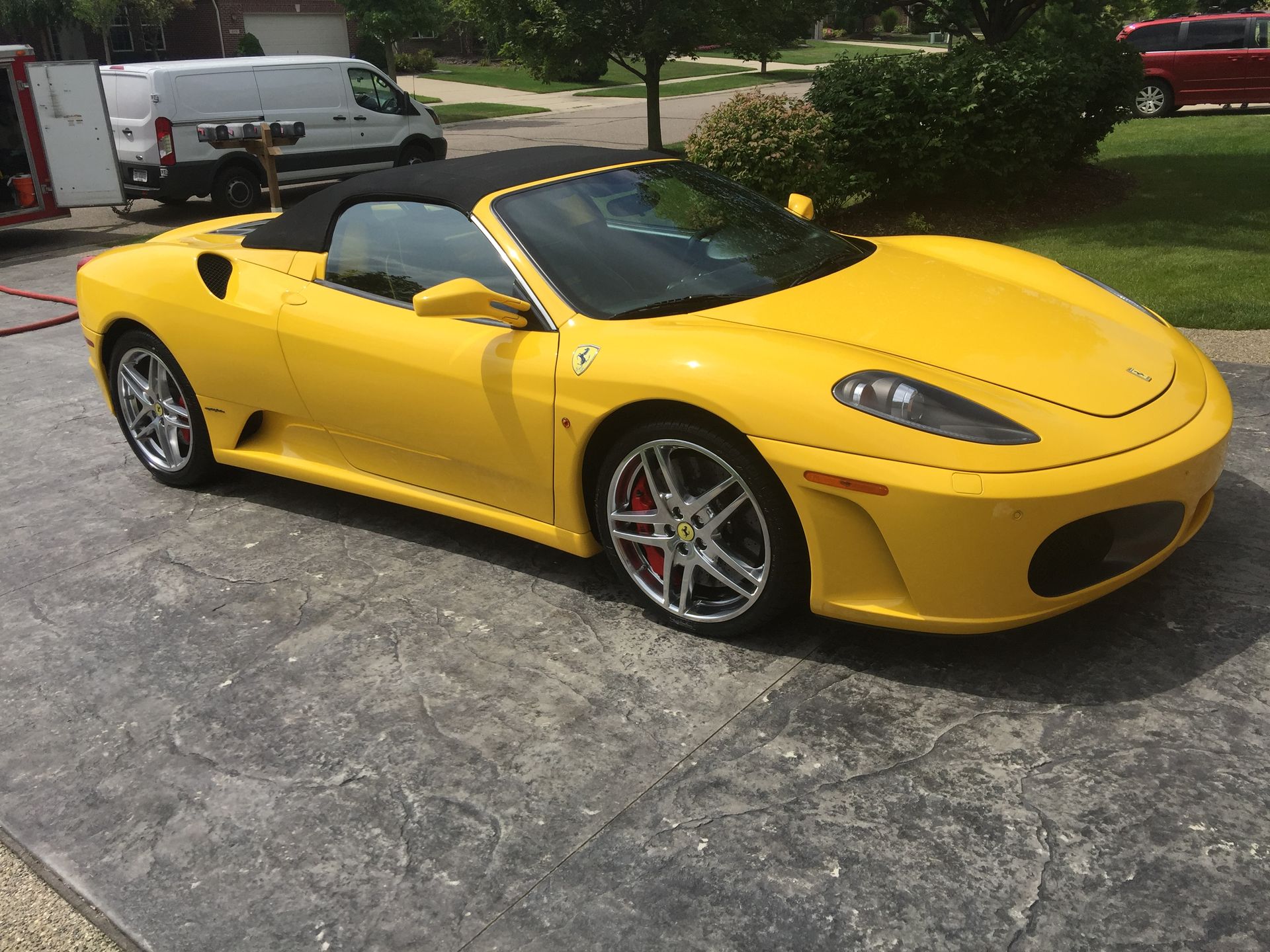 Yellow convertible sports car parked on a driveway with greenery in the background