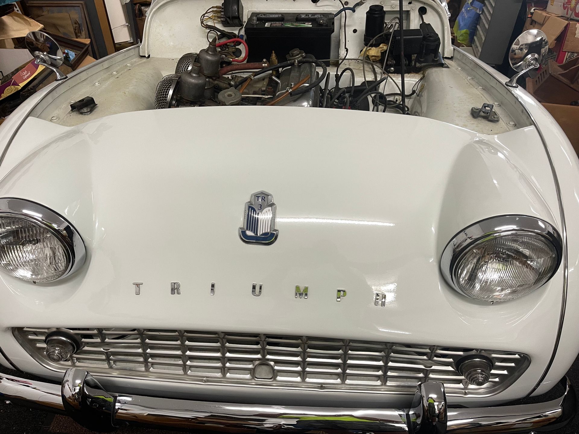 White Triumph sports car front end in a garage, hood open and engine exposed