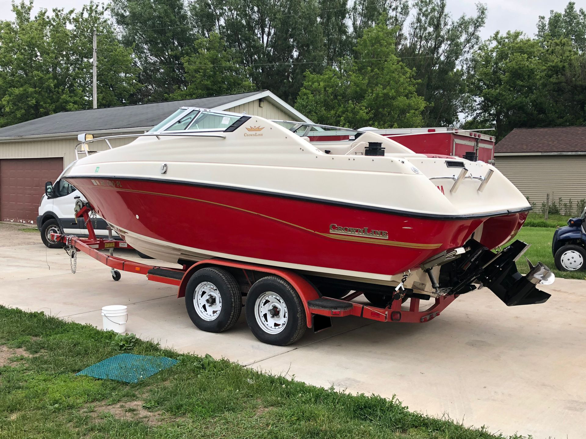 Red and white speedboat on a trailer parked in a driveway beside a garage