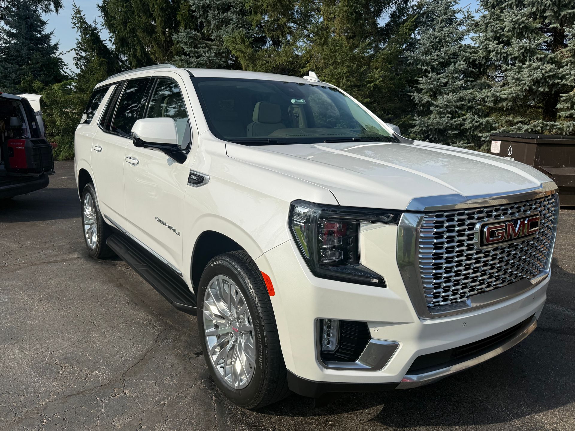 White GMC SUV parked outdoors on a driveway, front three-quarter view, with trees in the background