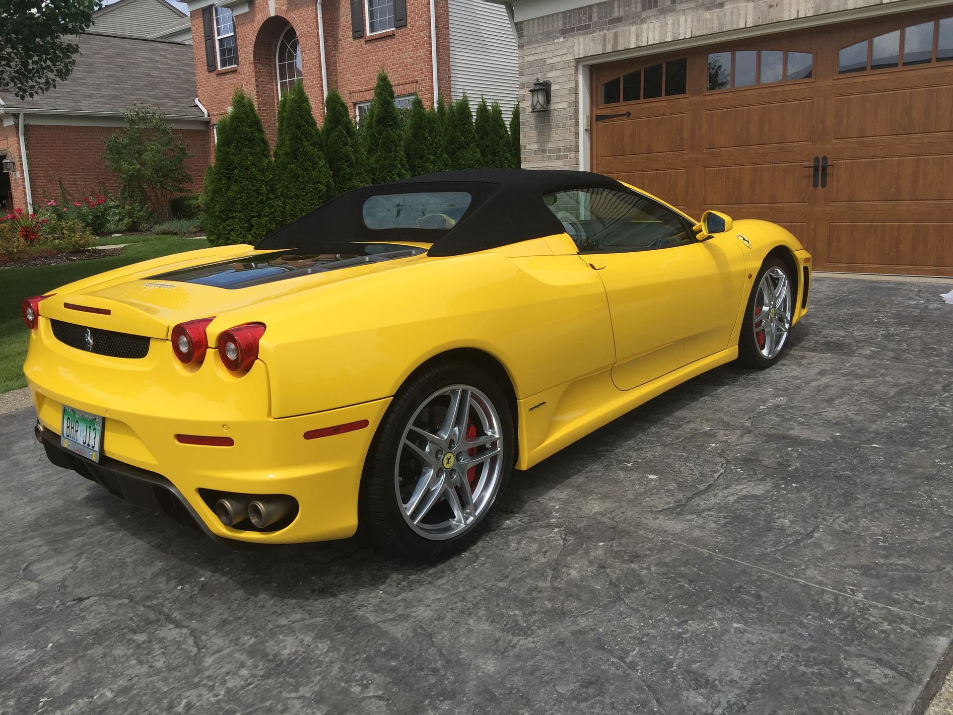 Bright yellow convertible sports car parked in a driveway beside a brick house.