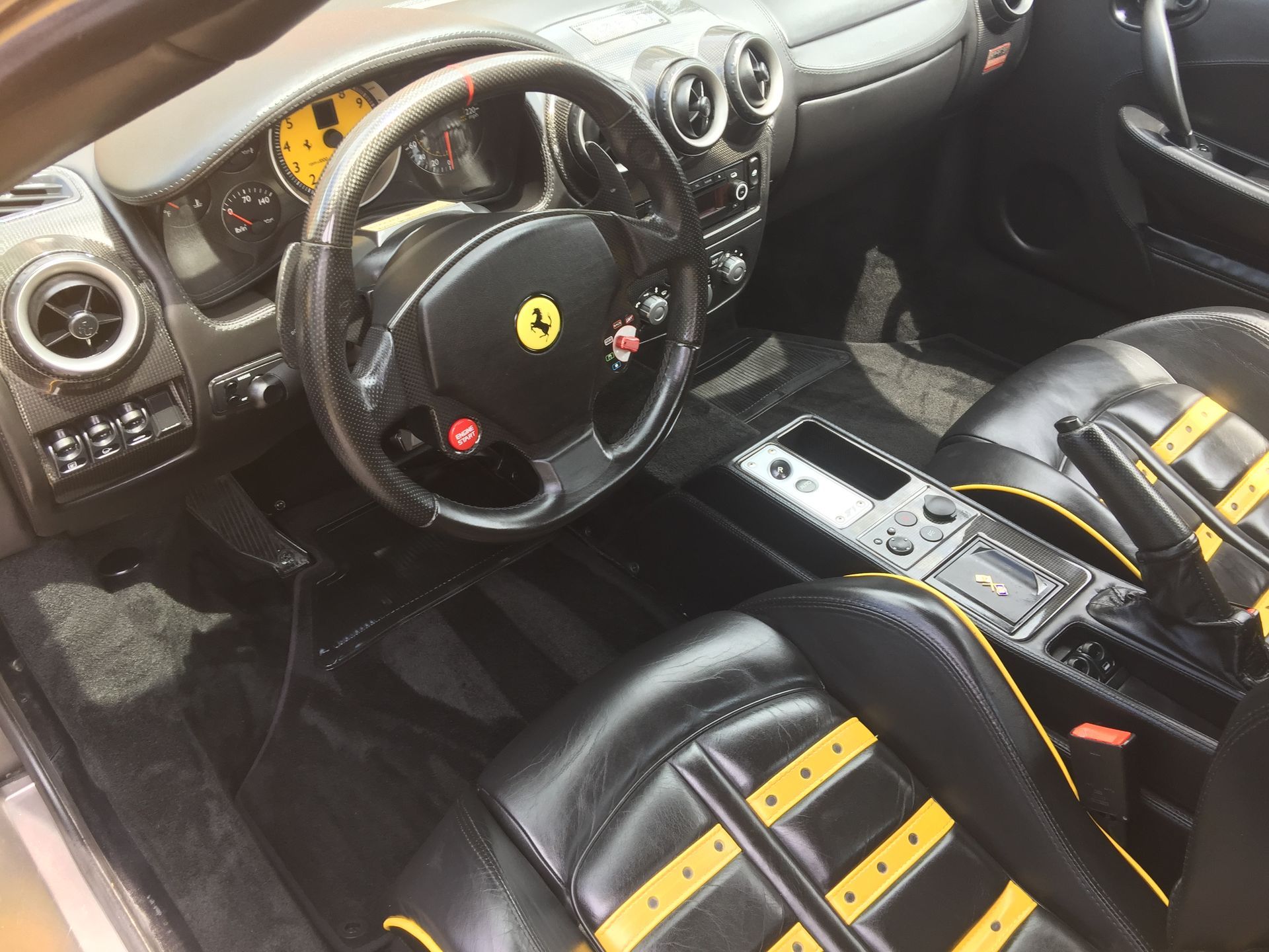 Black Ferrari interior with steering wheel, dashboard, and black-yellow racing seats