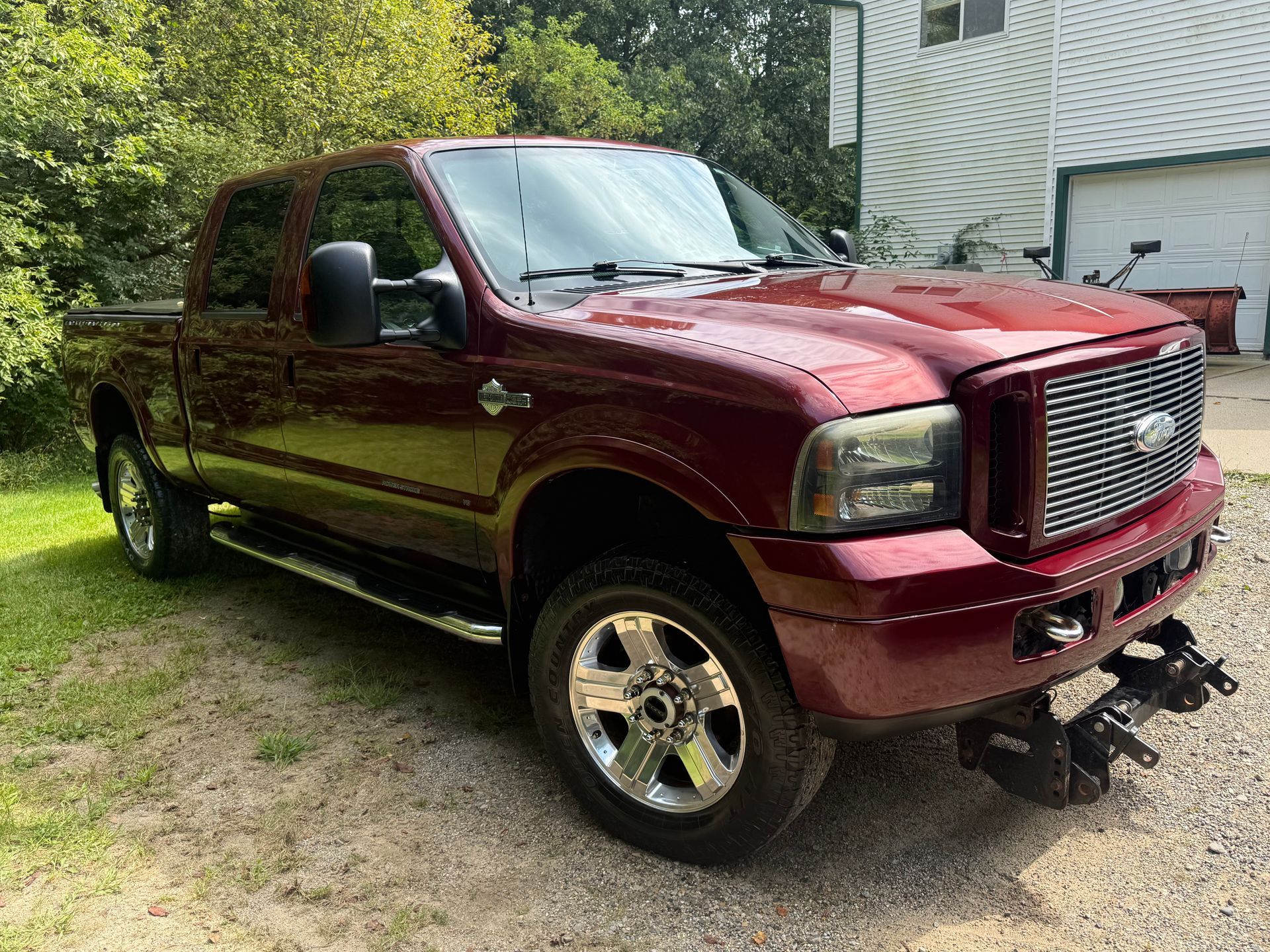 Maroon lifted pickup truck parked on a driveway beside a house and trees