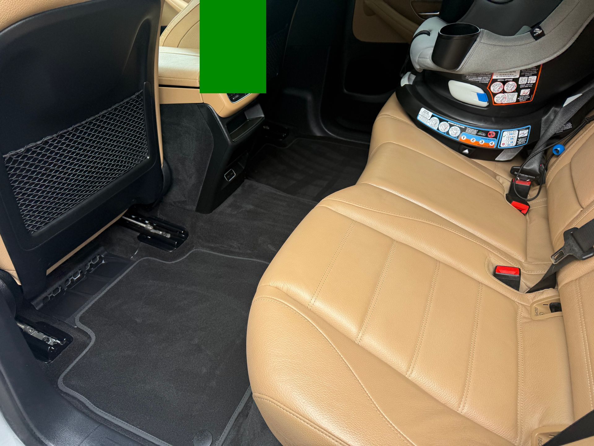 Car interior with tan leather back seat, black floor mats, and a child car seat base installed