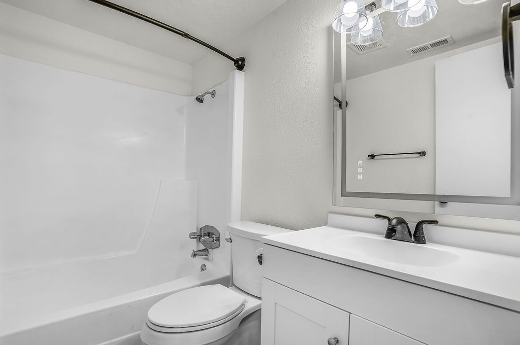 White bathroom with tub, toilet, vanity, and mirror. Black fixtures and hardware.